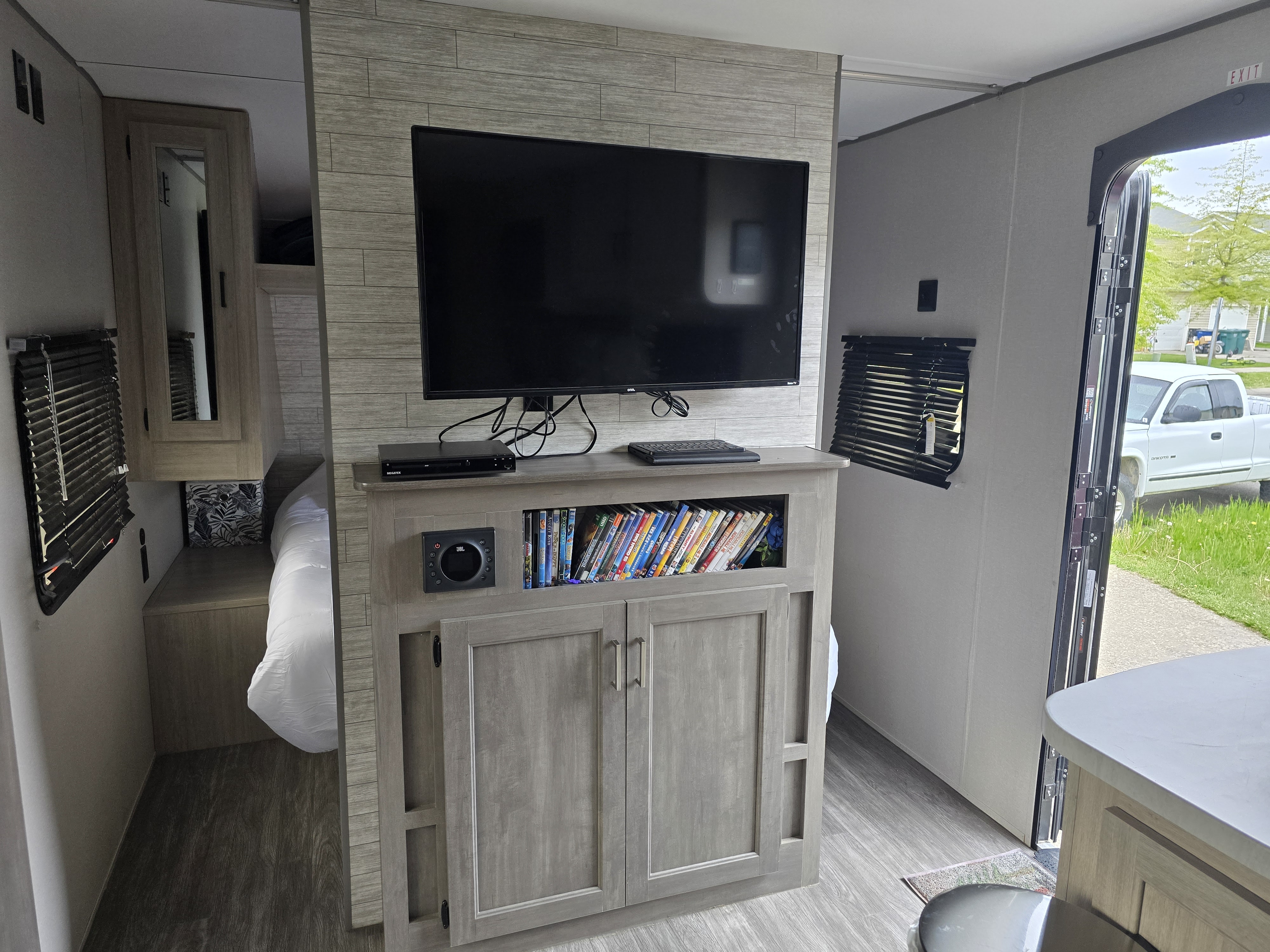 An RV rental interior featuring a TV entertainment center with JBL audio, DVD collection, a cozy bedroom, and kitchen counter.. Forest River Aurora Aurora 2024