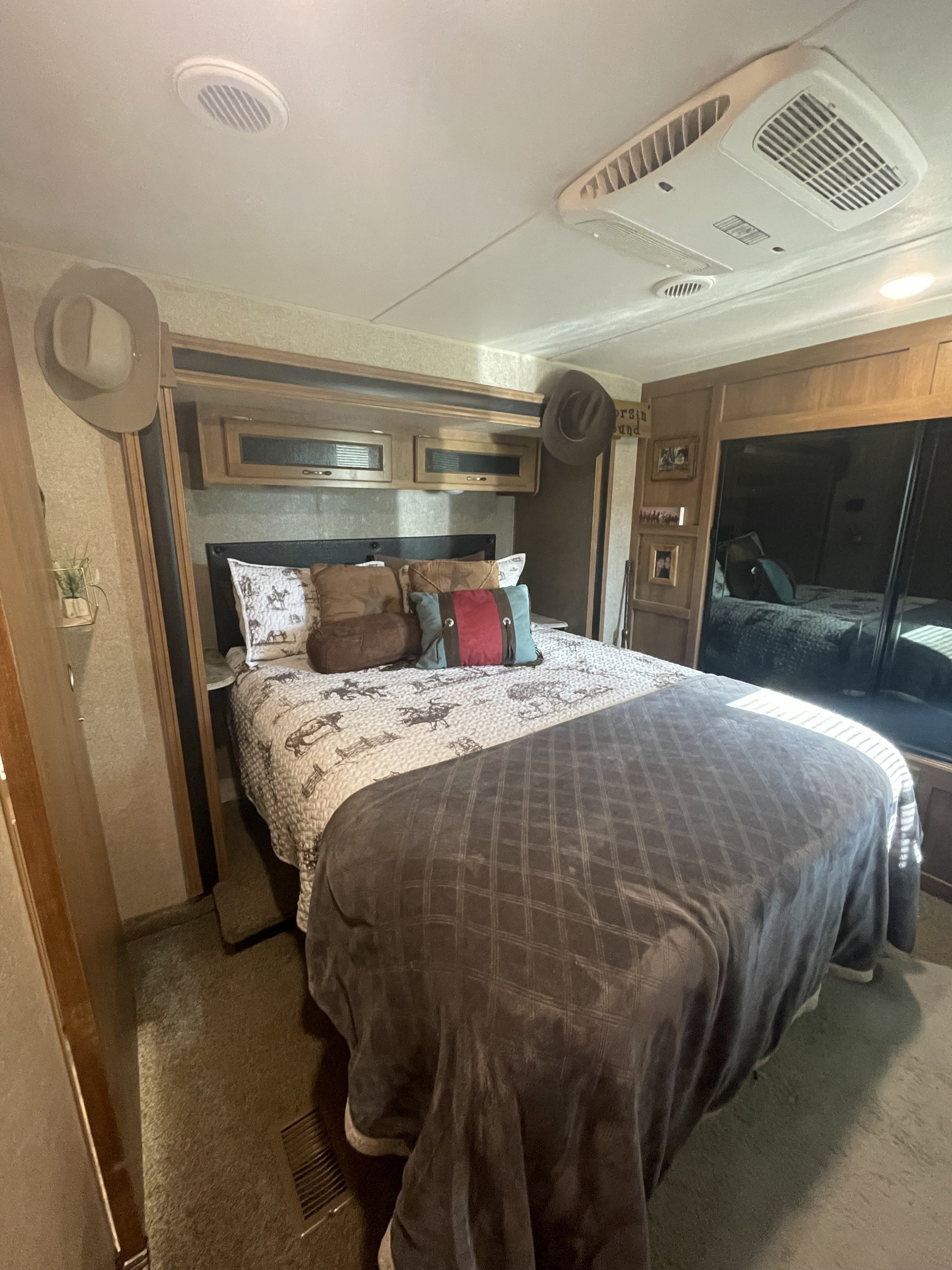 Cozy RV rental bedroom showcasing a comfy bed with western-themed bedding, overhead cabinets, and ceiling AC unit.. Coachmen 333RETS 2018