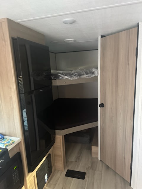 View inside an RV rental: includes bunk beds on the right, a black refrigerator on the left, and a small kitchen counter.. Keystone RV CM25B25 2025