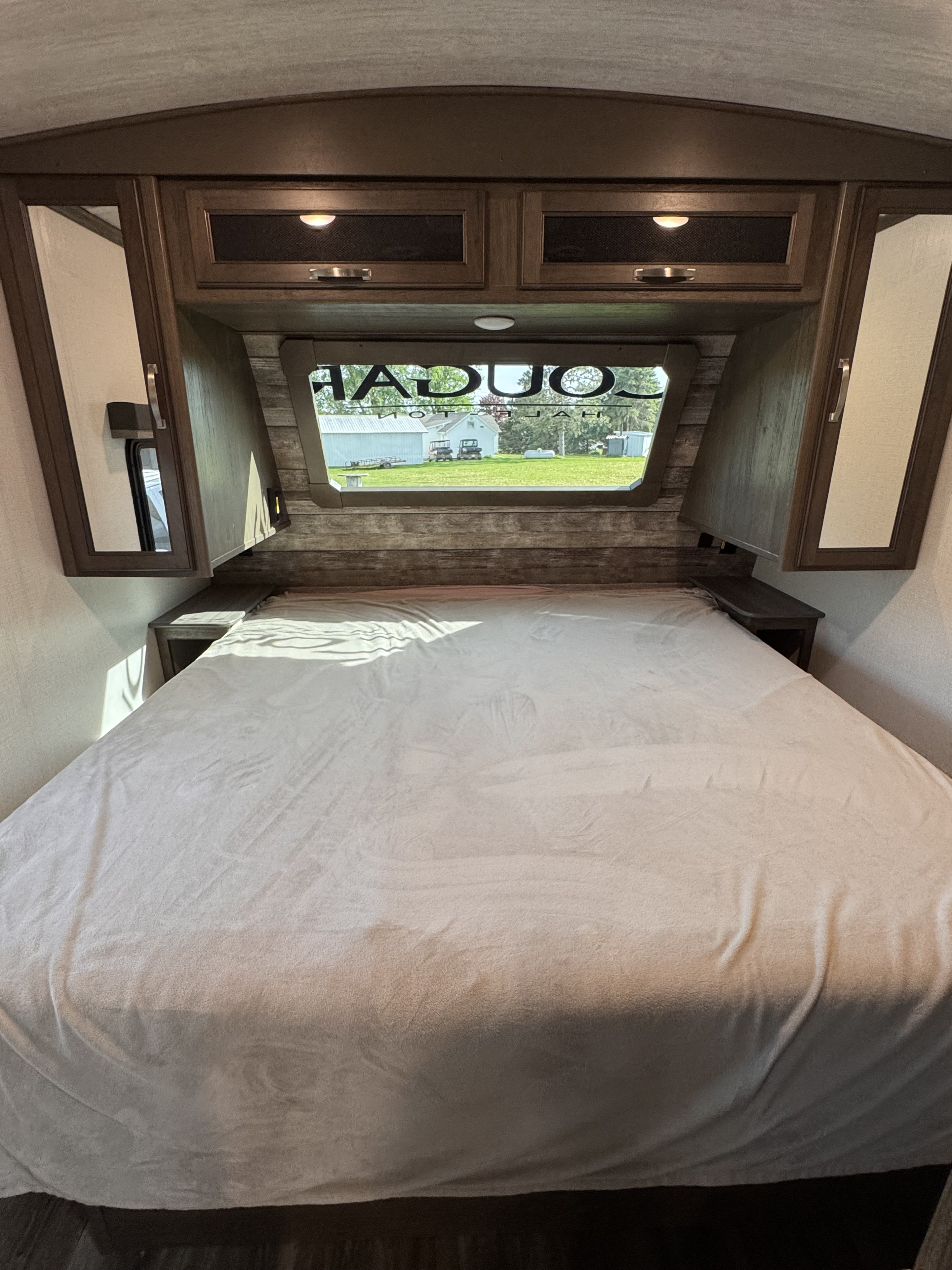 View of an RV rental bedroom, showing the bed, cabinetry with lighting, and a rear window with "Cougar" text.. Keystone RV Cougar 2022