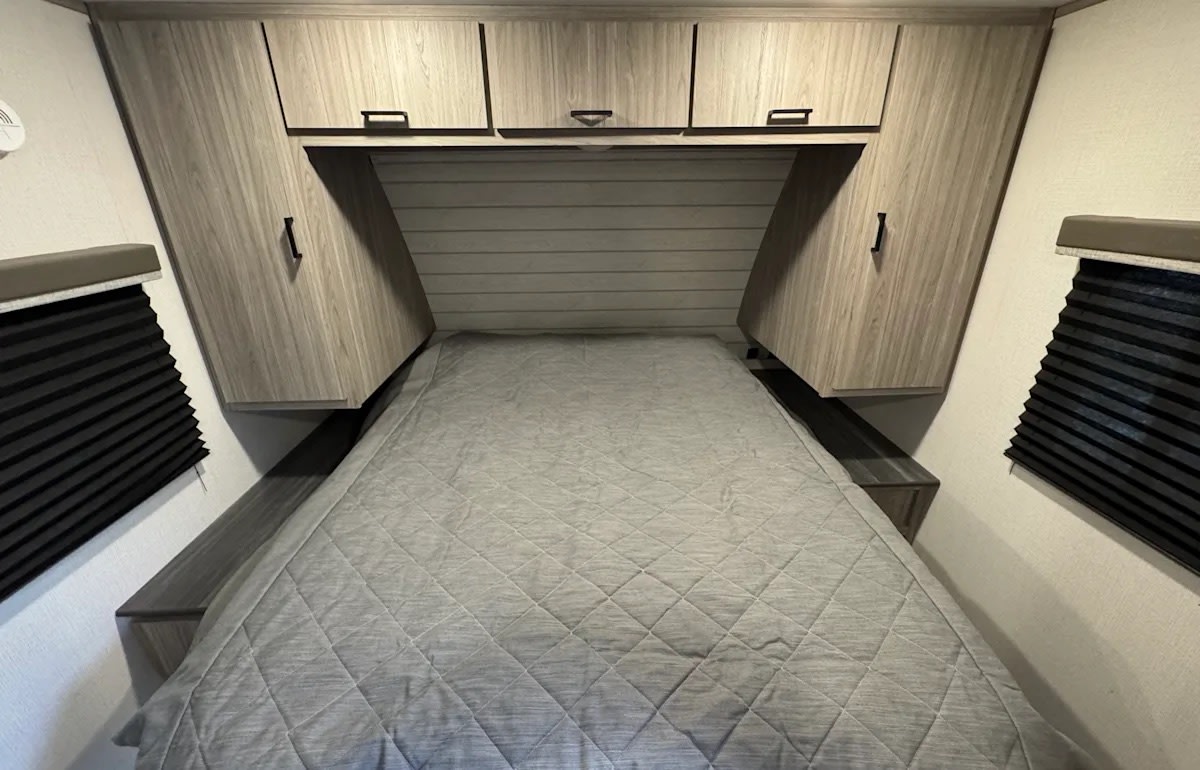Spacious RV rental bedroom featuring a bed, ample overhead/side cabinets, and window blinds for privacy.. Keystone RV Passport SL 2021