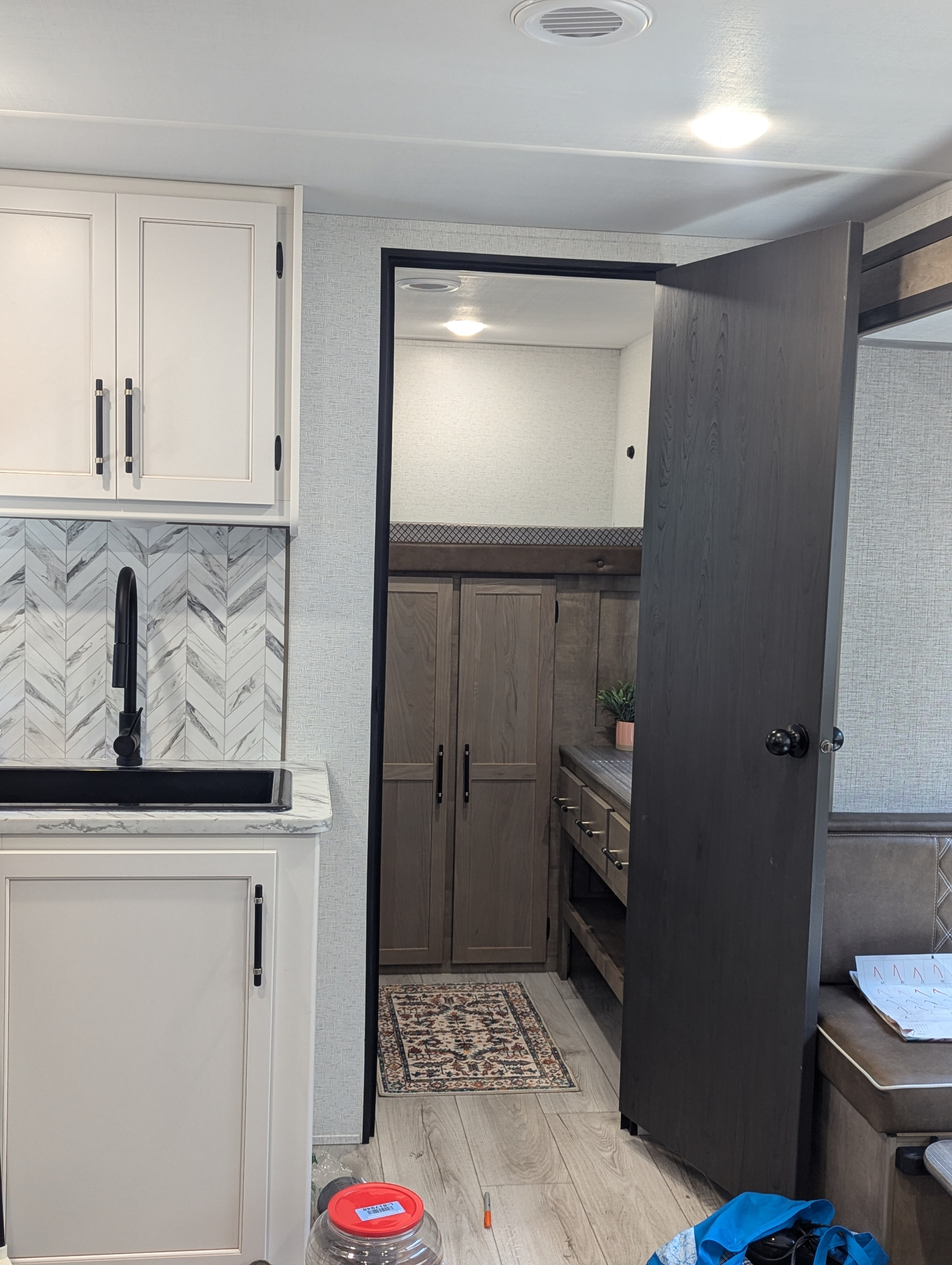 Inside this RV rental, find a modern kitchenette with white cabinets and herringbone backsplash, alongside a dark wood door opening to a bunk bed area.. Keystone Springdale Classic 291BRC 2025