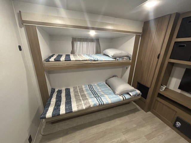 Inside an RV rental: a neat bunk room with two comfy beds, striped bedding, built-in storage, and a small TV.. Forest River Salem 2025