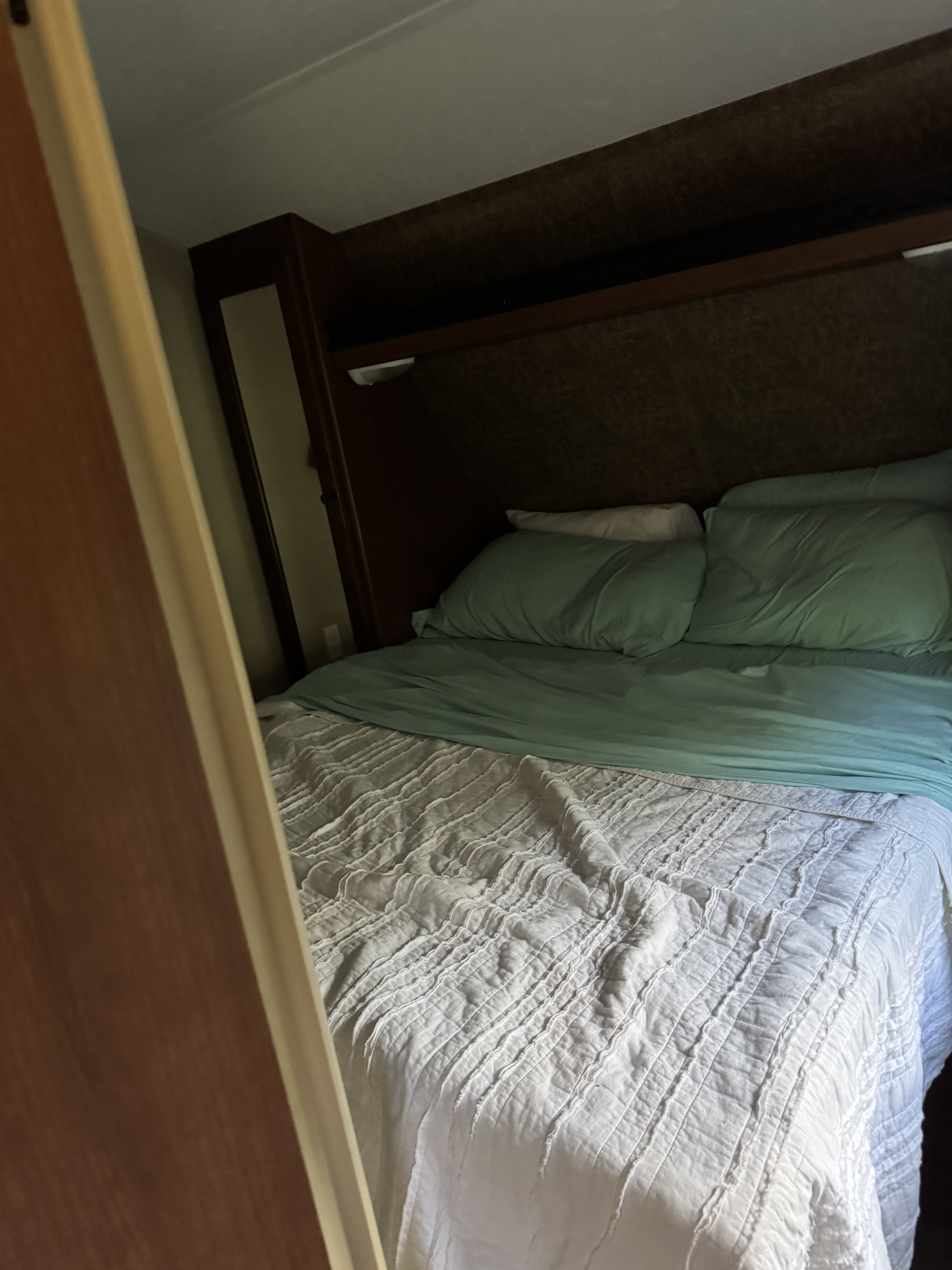 Cozy RV rental bedroom featuring a neatly made bed with teal and white bedding, built-in headboard, and overhead storage.. Aspen Trail Aspen Trail Trailer 2014
