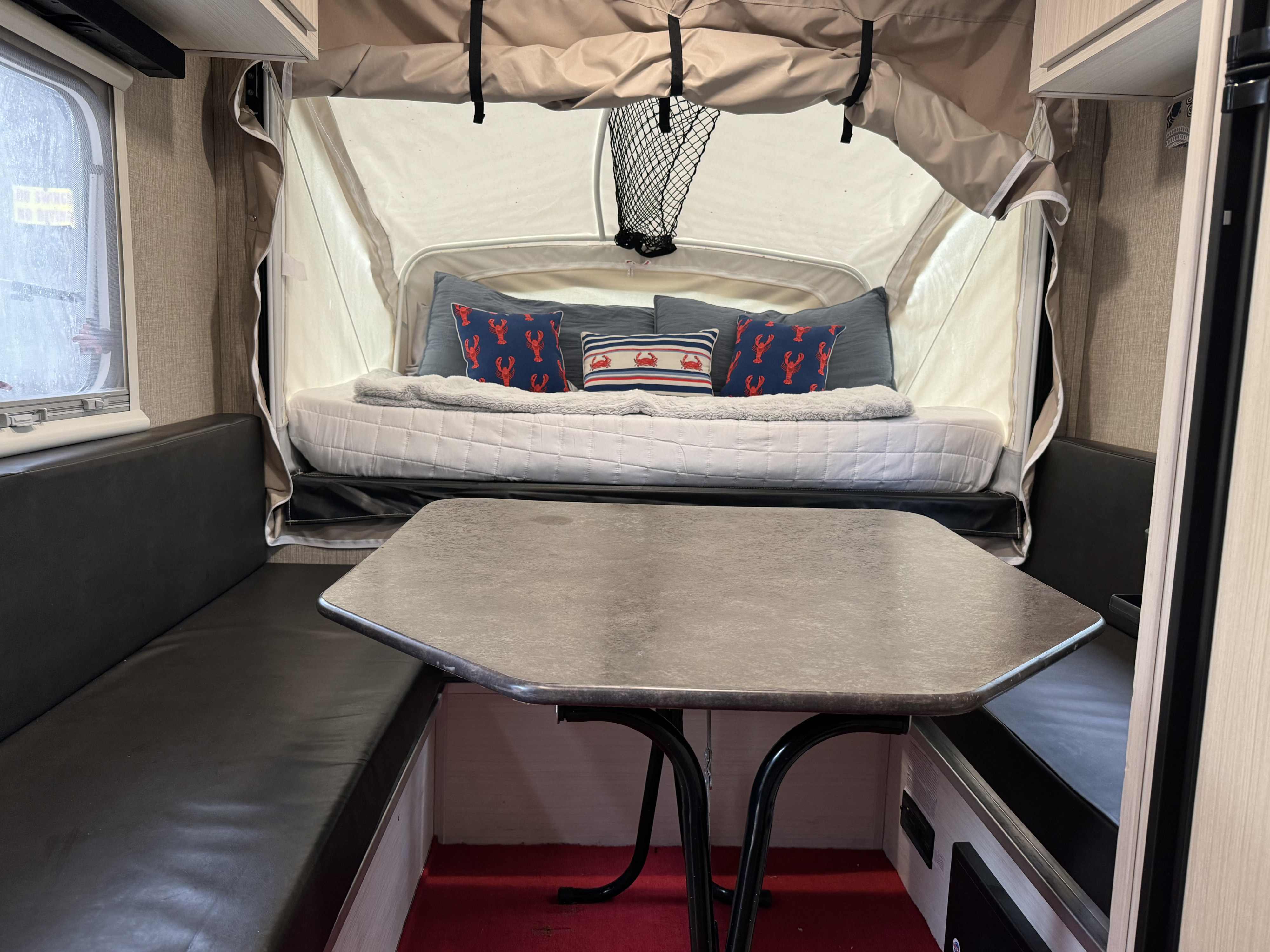 An RV rental's inviting interior: a central table, black booth seating, and a bed area with blue/red nautical pillows.. Camp Lite Camp Lite Trailer 2017