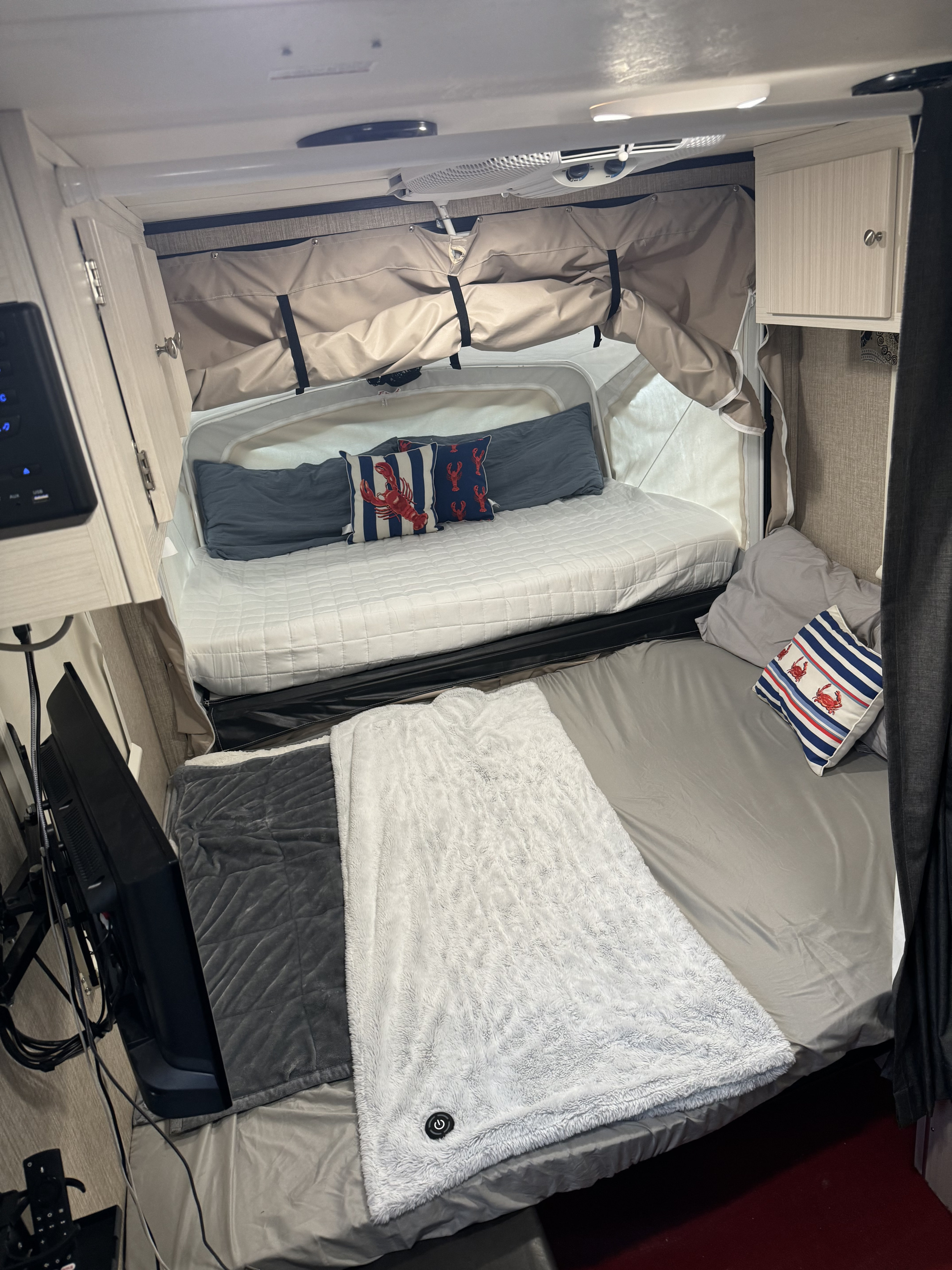 Inviting rv rental sleeping area with two beds: one pop-out, one standard. Cozy blankets, nautical pillows, TV, and cabinets visible.. Camp Lite Camp Lite Trailer 2017