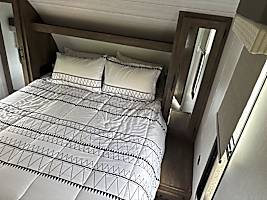 Comfortable RV rental bedroom. White bedding with black geometric patterns, overhead shelf, and mirrored wardrobes. Ideal for travel.. Forest River Wildwood X-Lite 2022