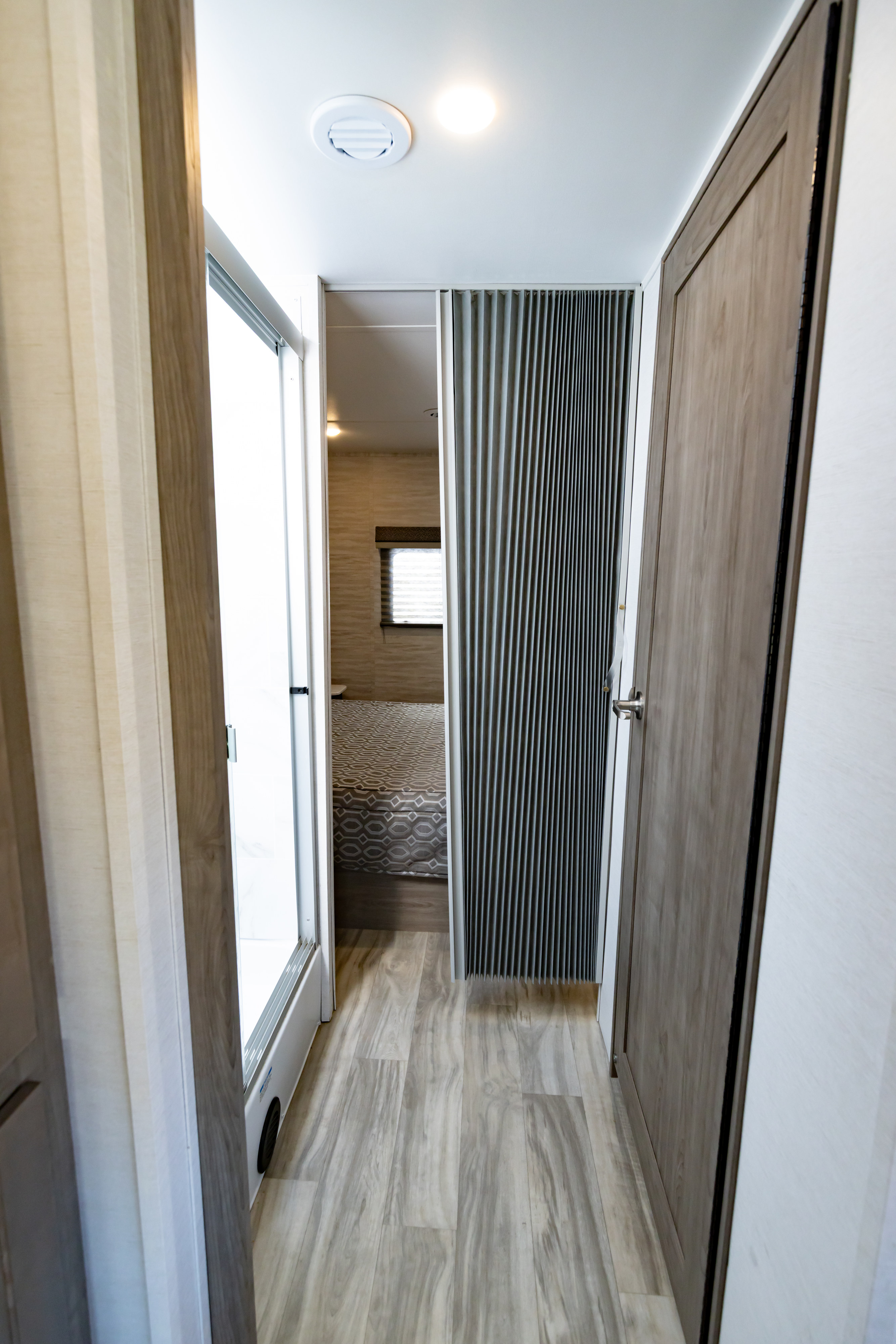 RV rental: A bright, narrow hallway with light wood-look flooring. On the left, an open shower. Ahead, a bedroom with a bed. Right, a closed door.. Gulf Stream Conquest 2023