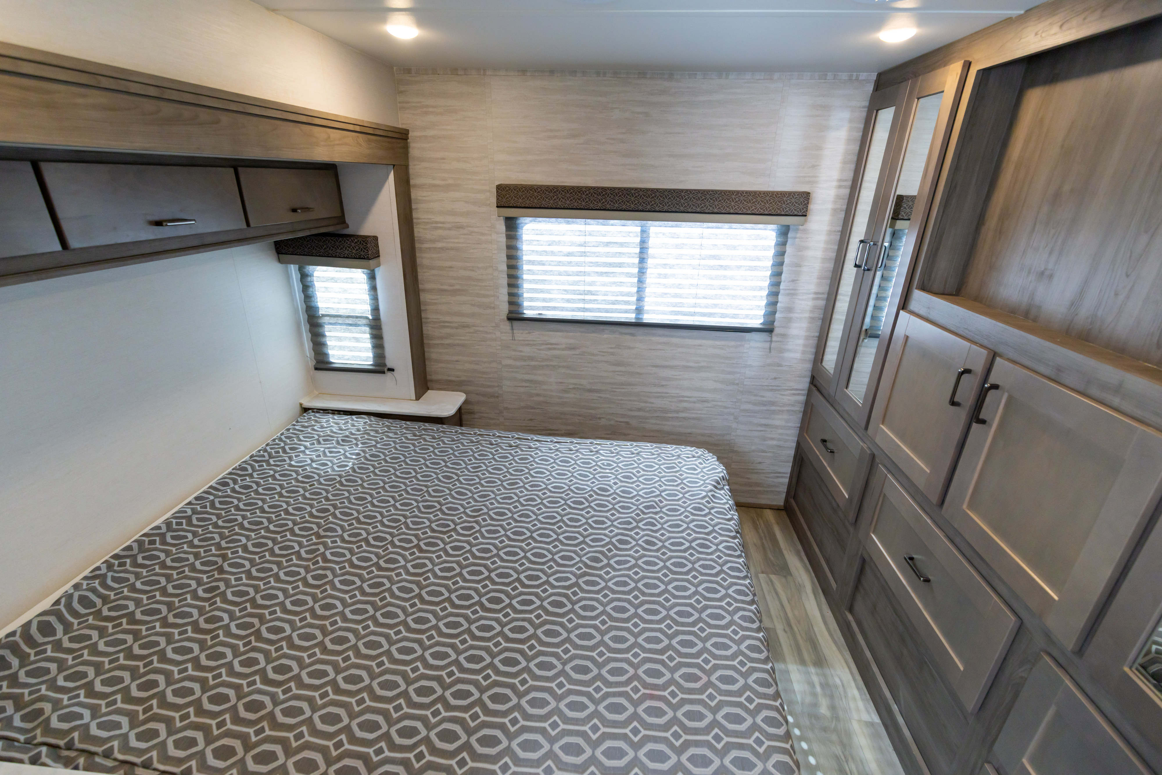 Modern RV rental bedroom featuring a patterned bed, overhead cabinets, two windows, and a large mirrored wardrobe.. Gulf Stream Conquest 2024