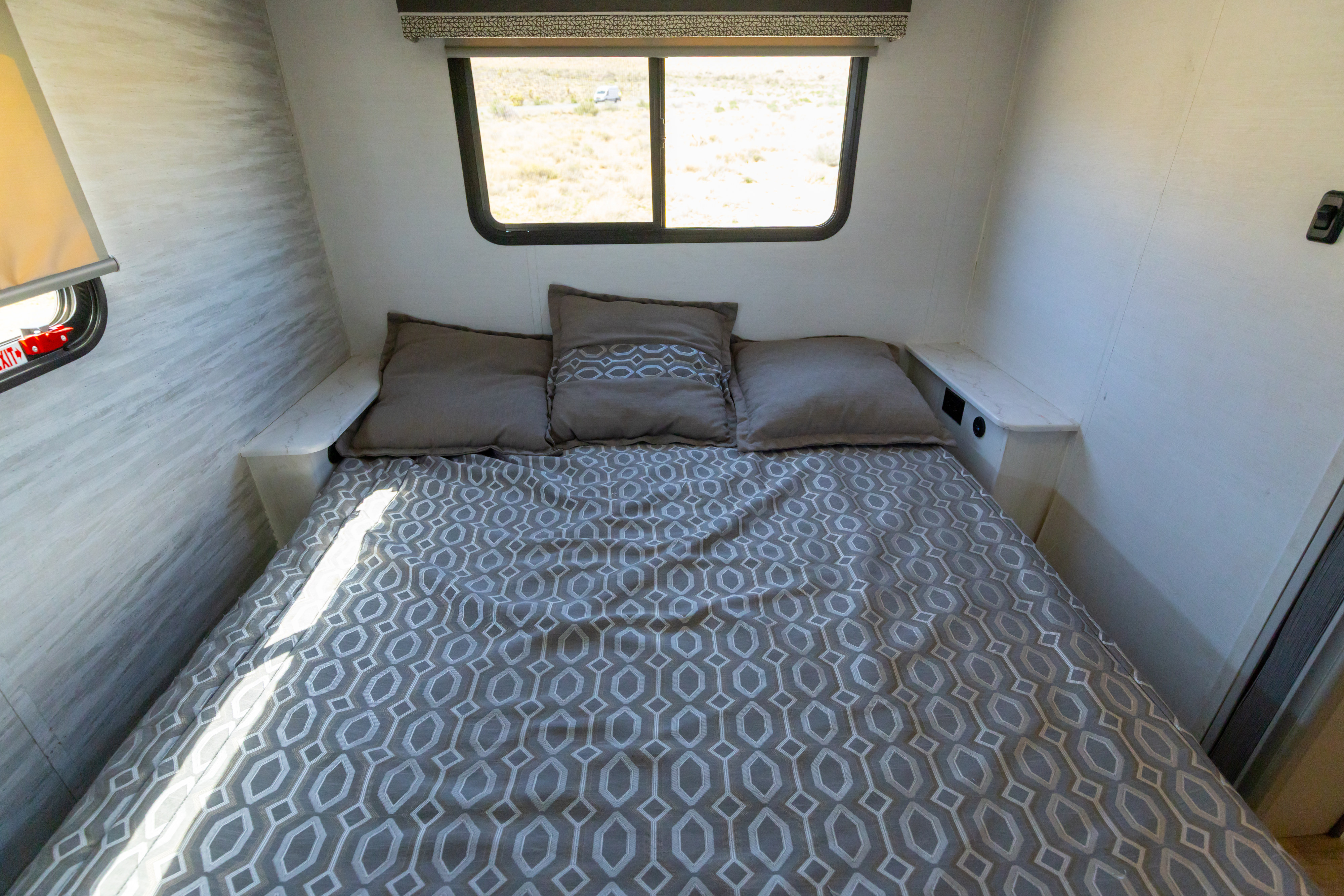 Cozy RV rental bedroom with patterned bedding, compact nightstands, and a window view of the desert landscape.. Gulf Stream Conquest 2024