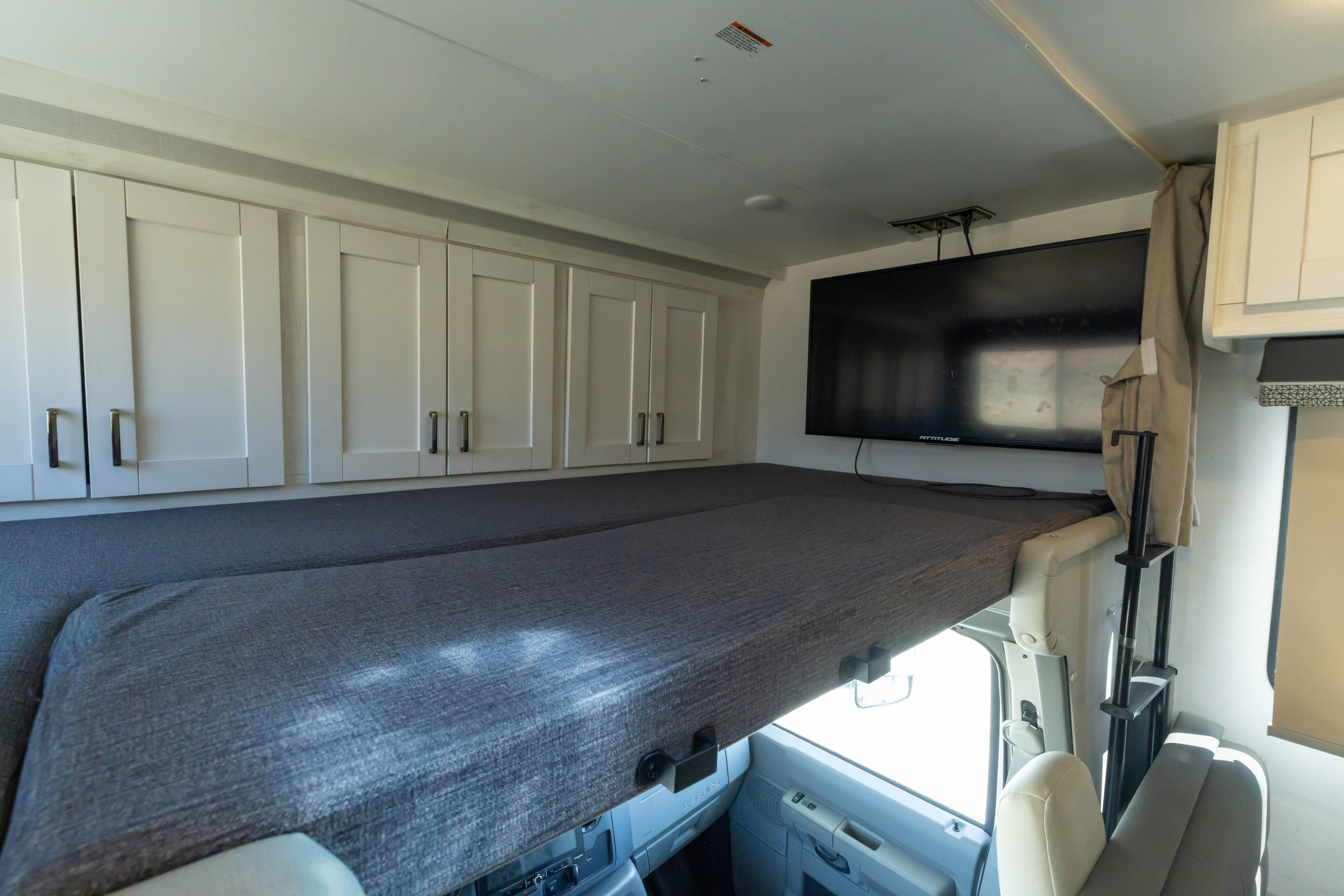 RV rental: Cab-over bunk with gray mattress, white overhead cabinets & TV. Ideal for comfy travel lodging.. Gulf Stream Conquest 2024