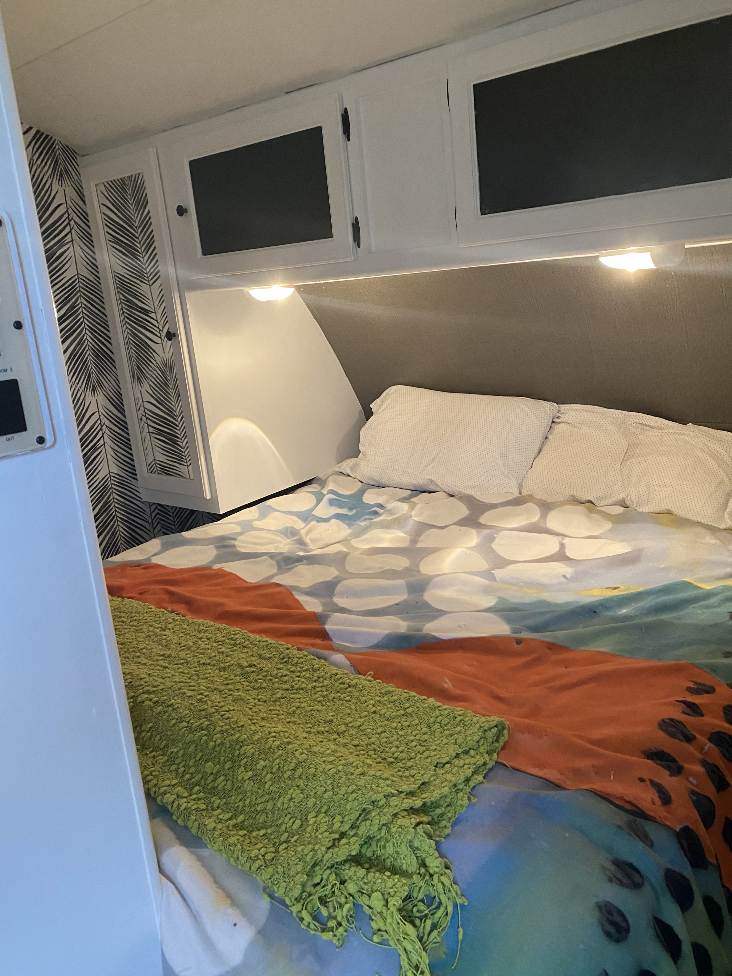 Cozy RV rental bedroom with colorful bedding, overhead cabinets, and stylish palm leaf wallpaper.. Keystone RV Bullet Ultra Lite 2014
