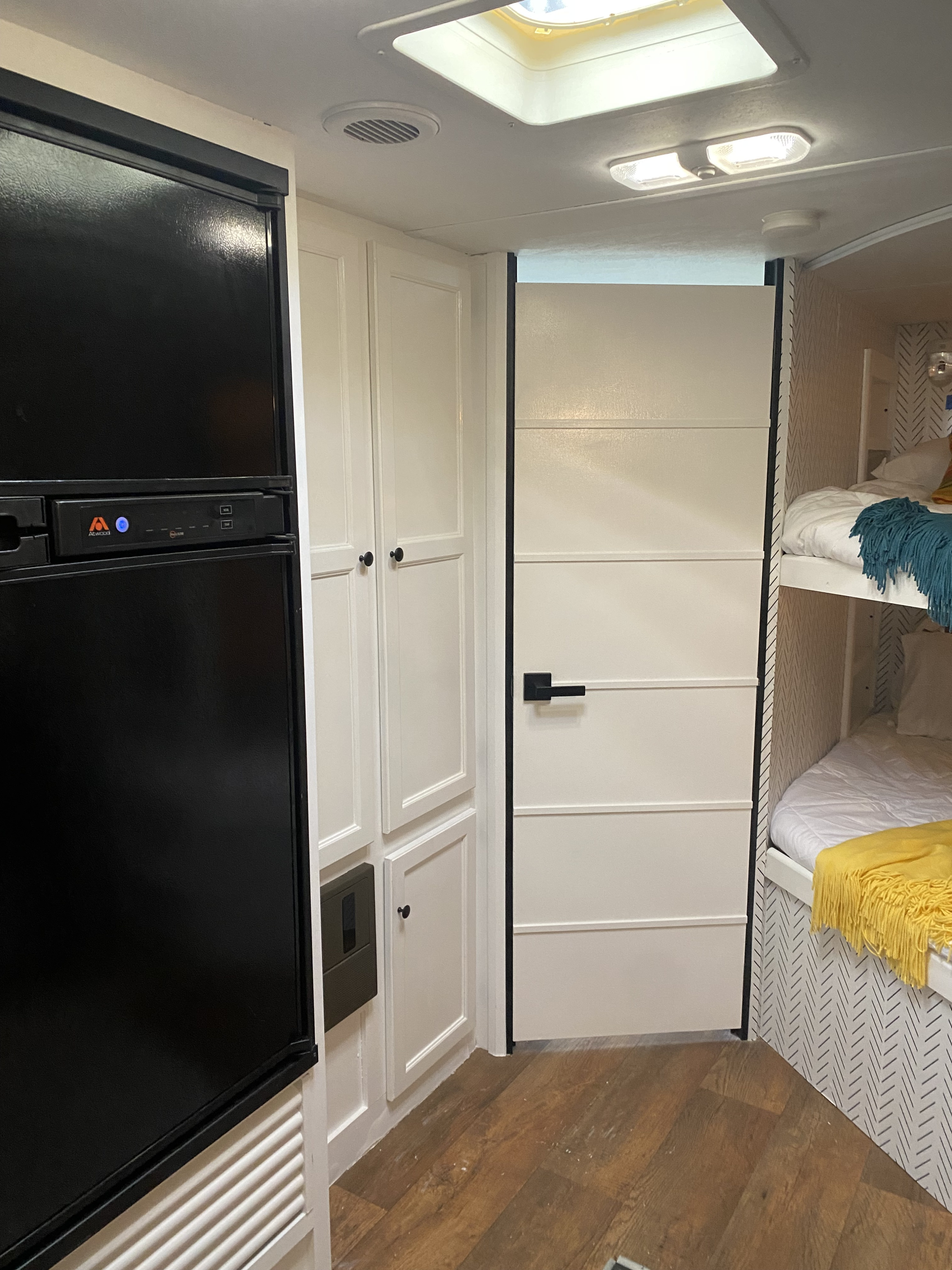 Modern RV rental interior with black fridge, white cabinets, sleek door, and cozy bunk beds with patterned walls.. Keystone RV Bullet Ultra Lite 2014