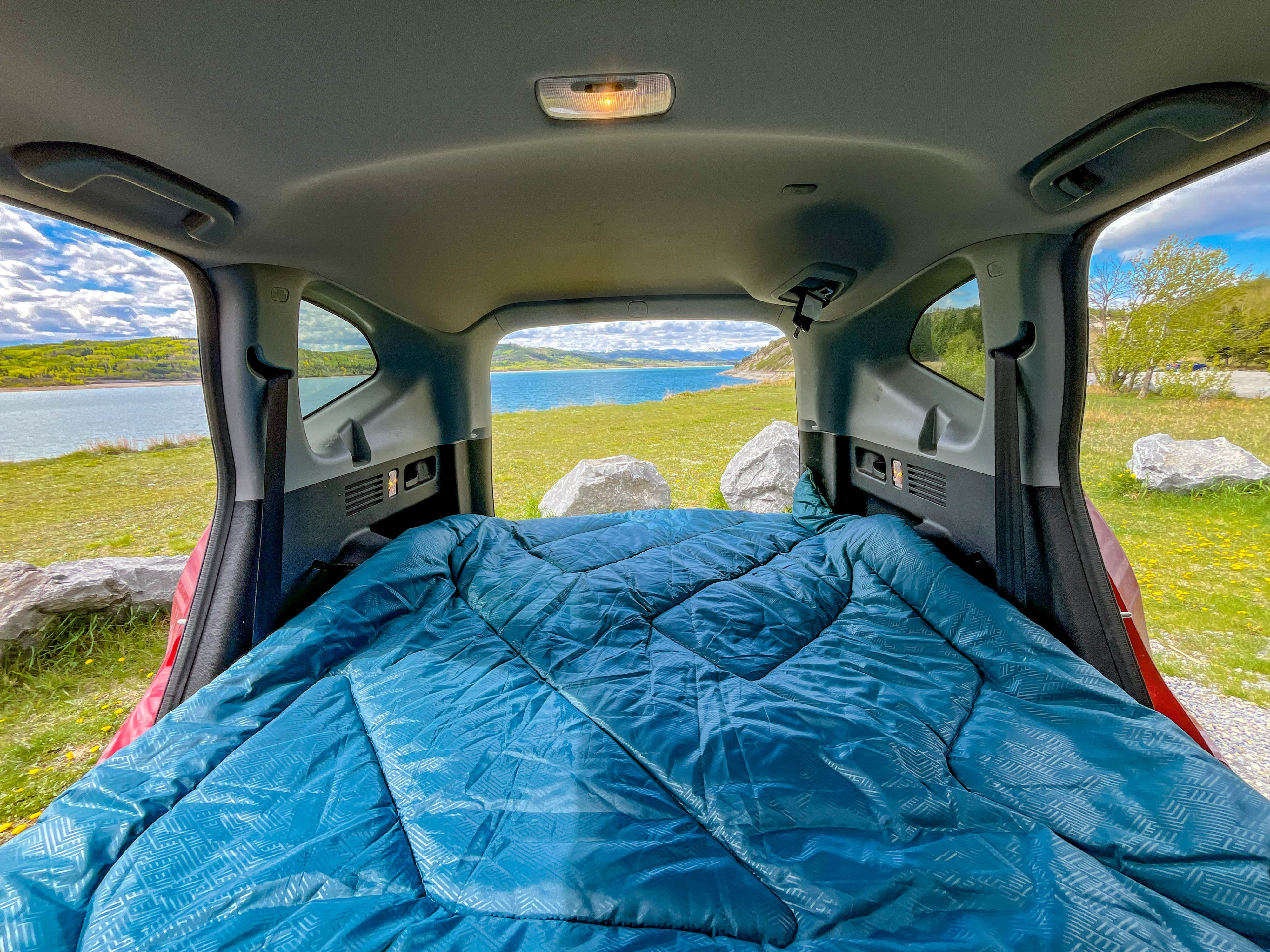 Cozy vehicle RV rental setup, showing a blue sleeping area overlooking a tranquil lake and green landscape.. honda 2019 CRV Red 2019