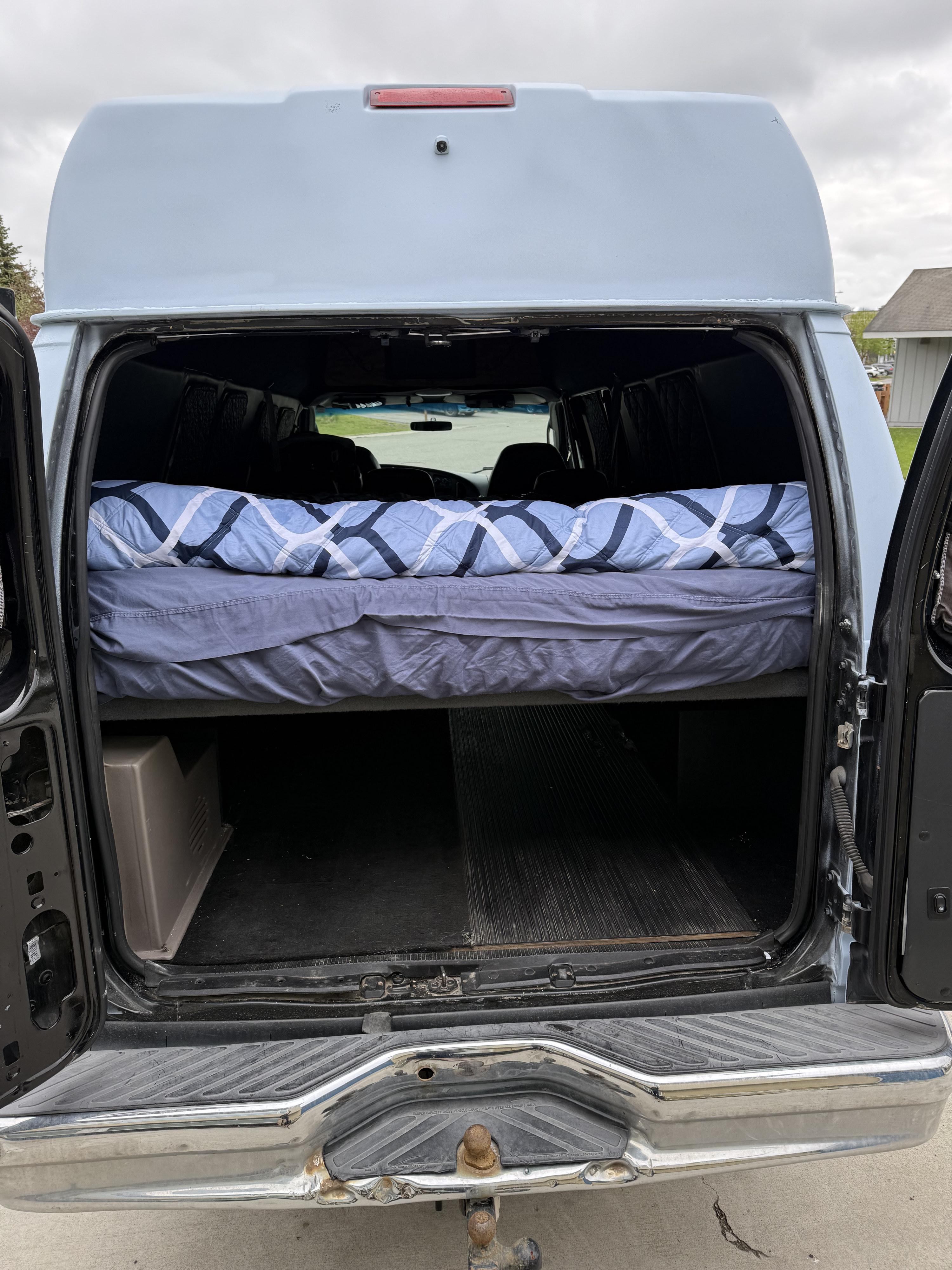 High-top van rv rental: converted interior with elevated bed & storage, seen through open rear doors. Tow hitch visible.. Ford E350 Super Duty 1-ton Camper Van 2006