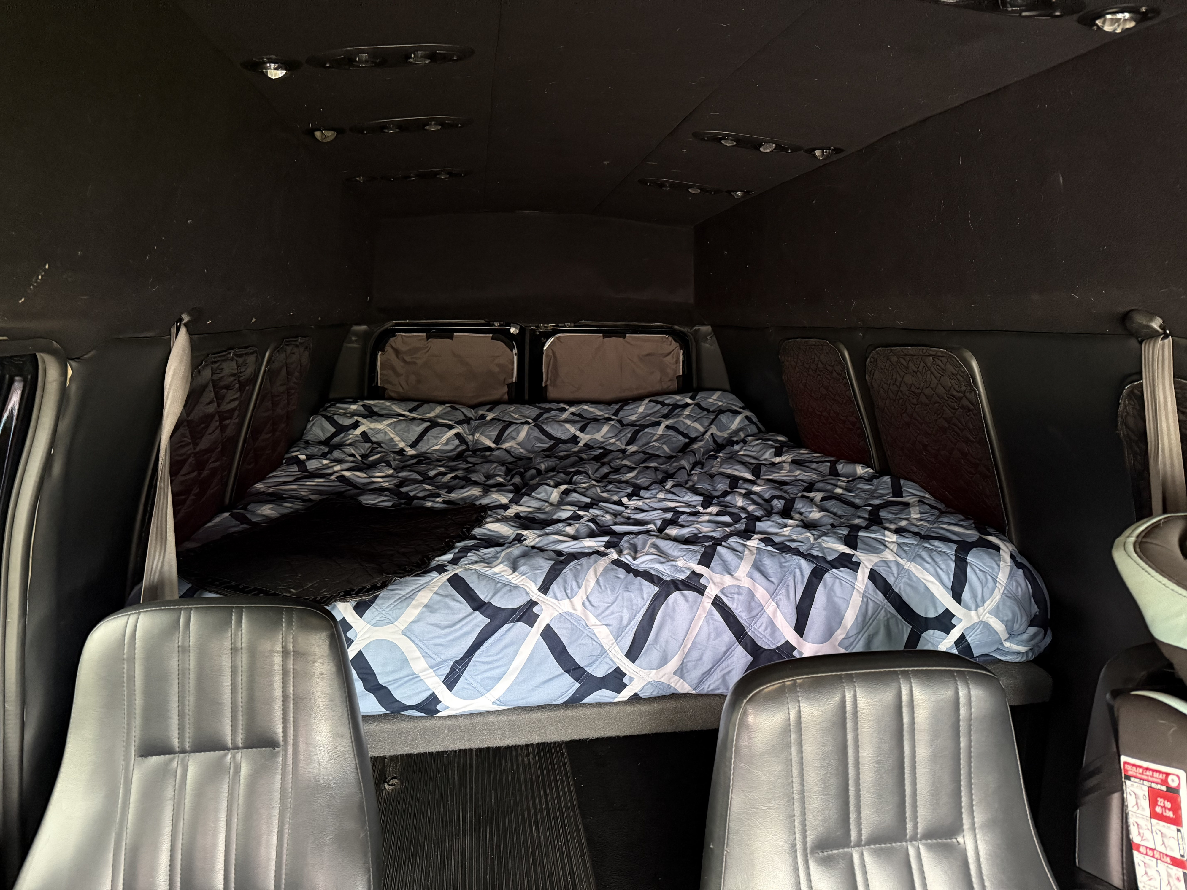 Cozy RV rental interior with a comfortable bed and front seating, ideal for mobile adventures and road trips.. Ford E350 Super Duty 1-ton Camper Van 2006