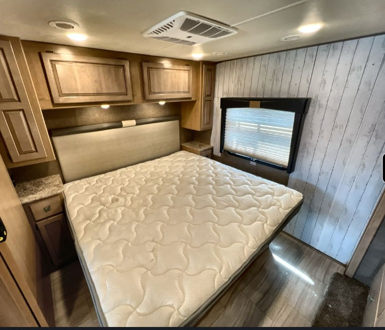 RV rental master bedroom showing a queen bed, light wood cabinets, and bright interior lighting.. Thor Windsport 2019