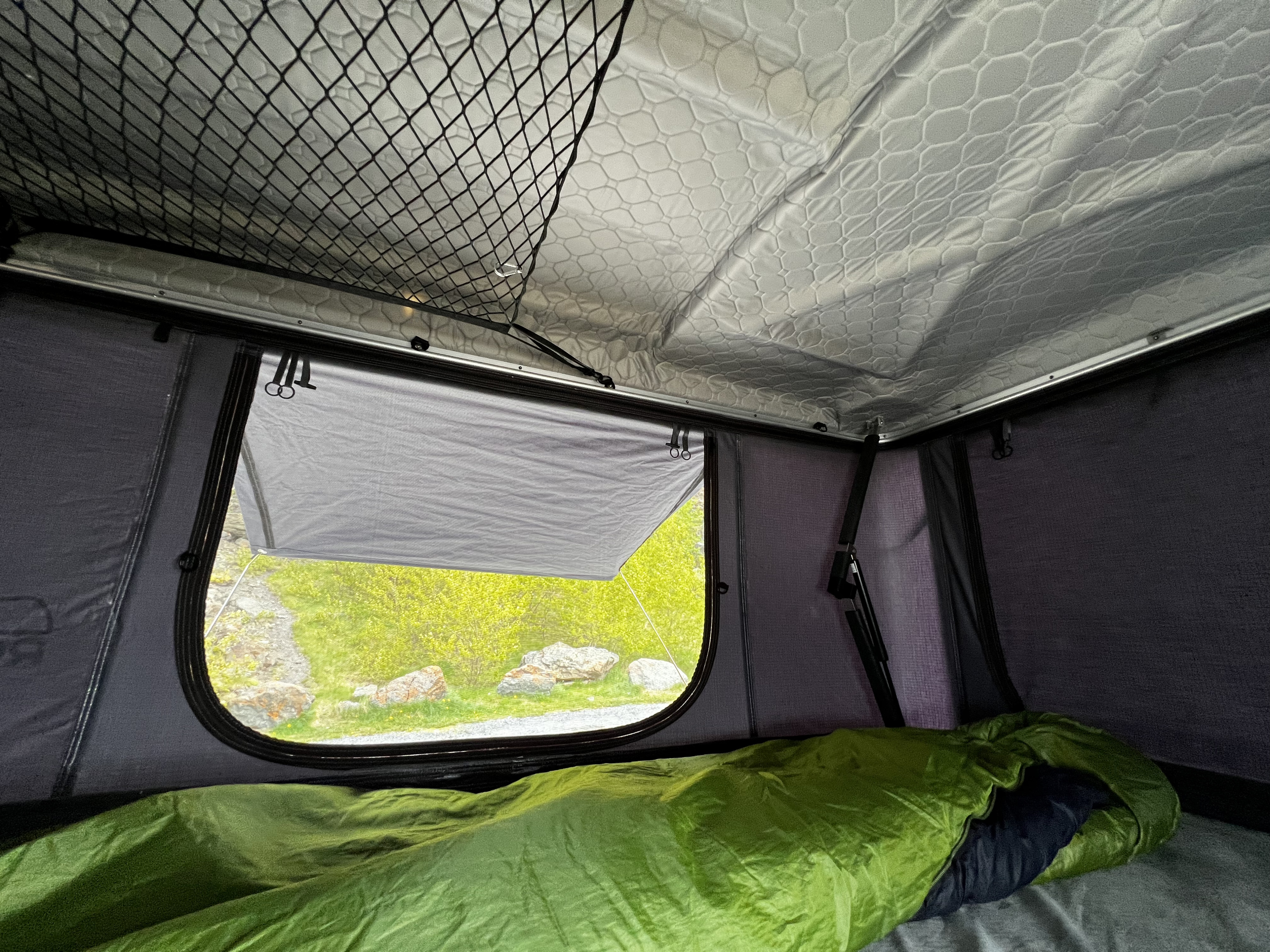Cozy view from an RV rental's rooftop tent, featuring a green sleeping bag and nature outside the open window.. Chevrolet Suburban 2015