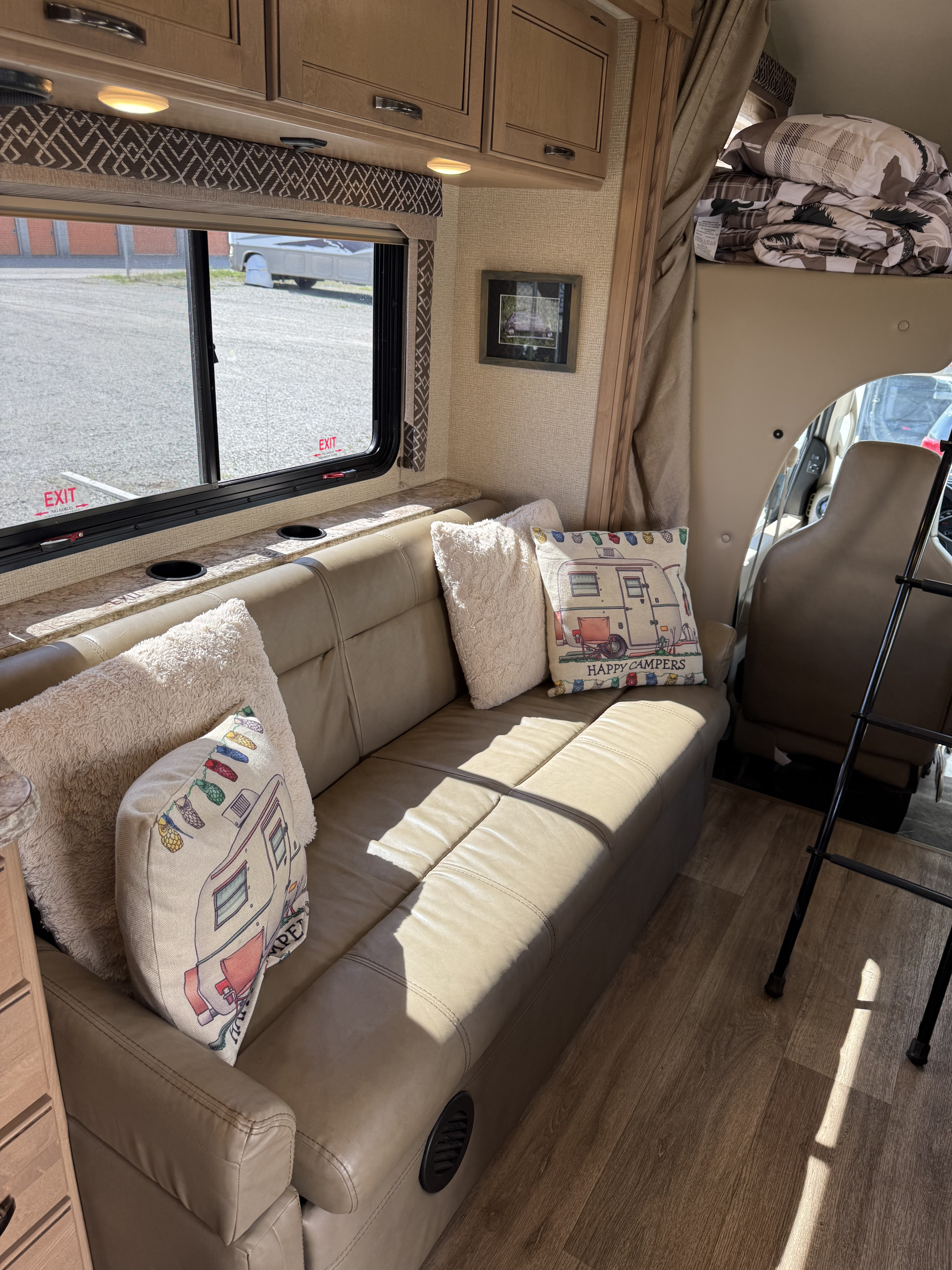 Step inside this rv rental! A comfy tan couch with fun camper pillows, large window, and overhead sleeping space.. Thor Four Winds 2018
