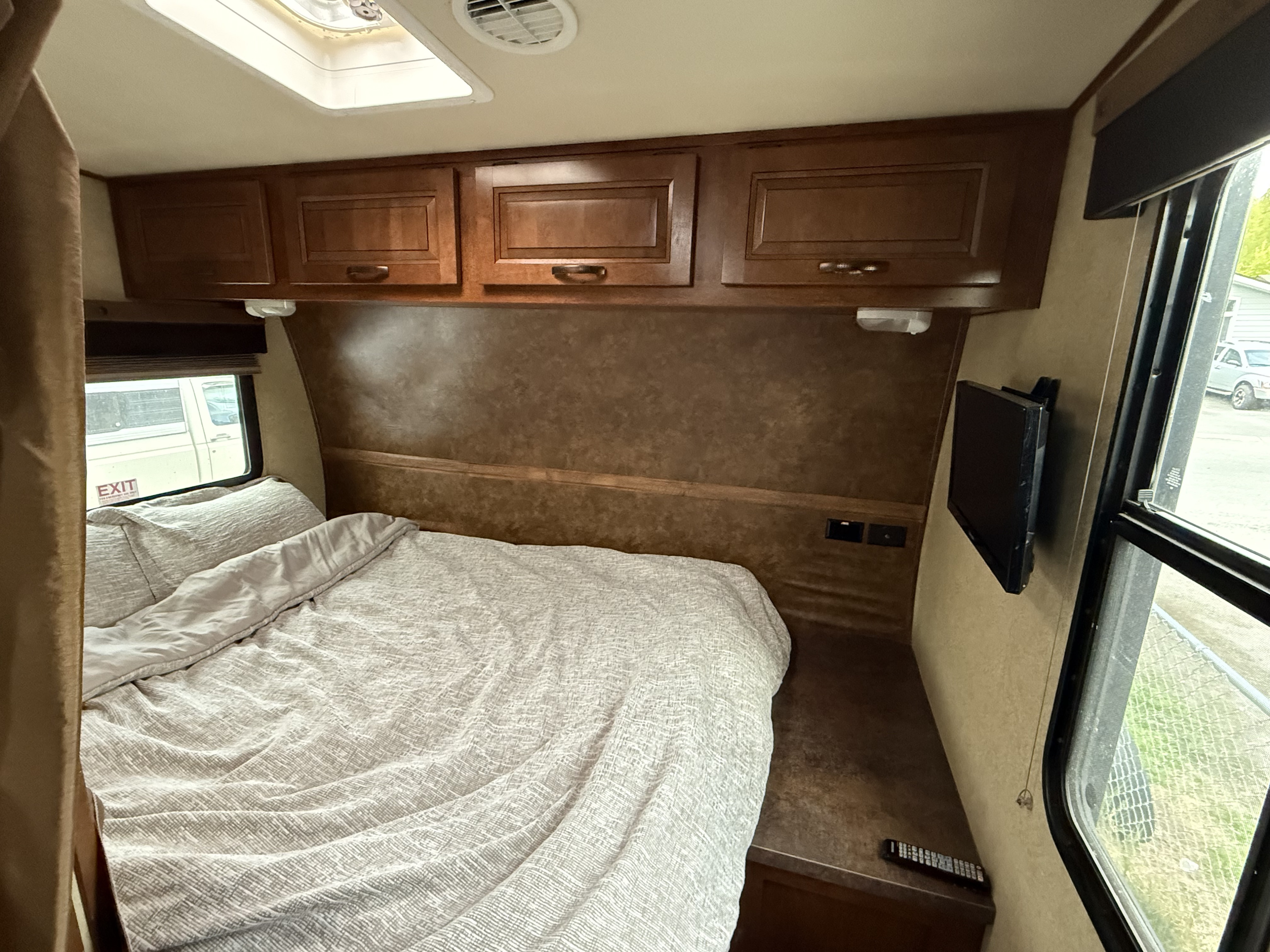 Comfortable RV rental bedroom with textured bedding, overhead cabinets, and a wall-mounted TV.. Forest River M-27HFS 2013