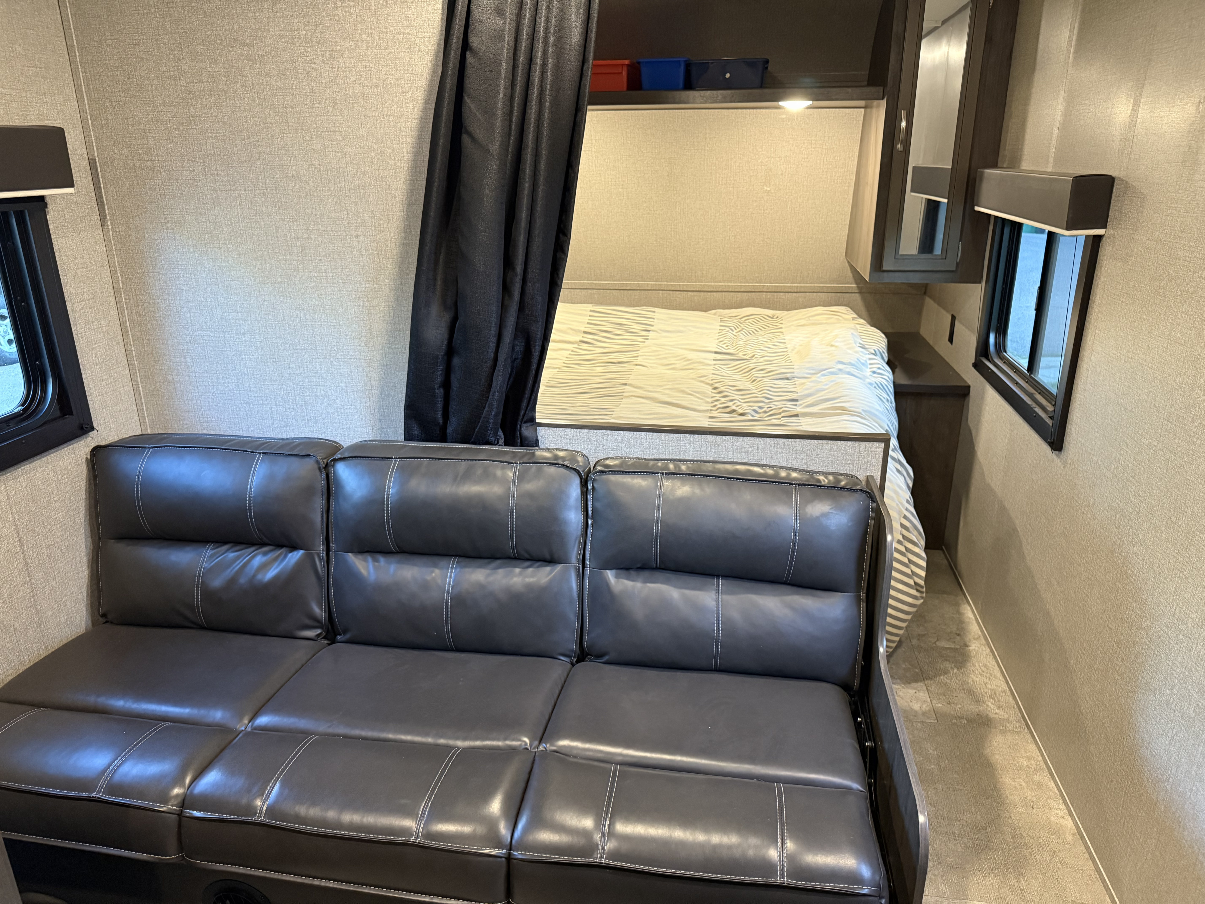 Inside this RV rental, find a comfortable grey sofa, pull-down curtain, and cozy bed. Practical layout for your next adventure.. Jayco Jay Flight 2020