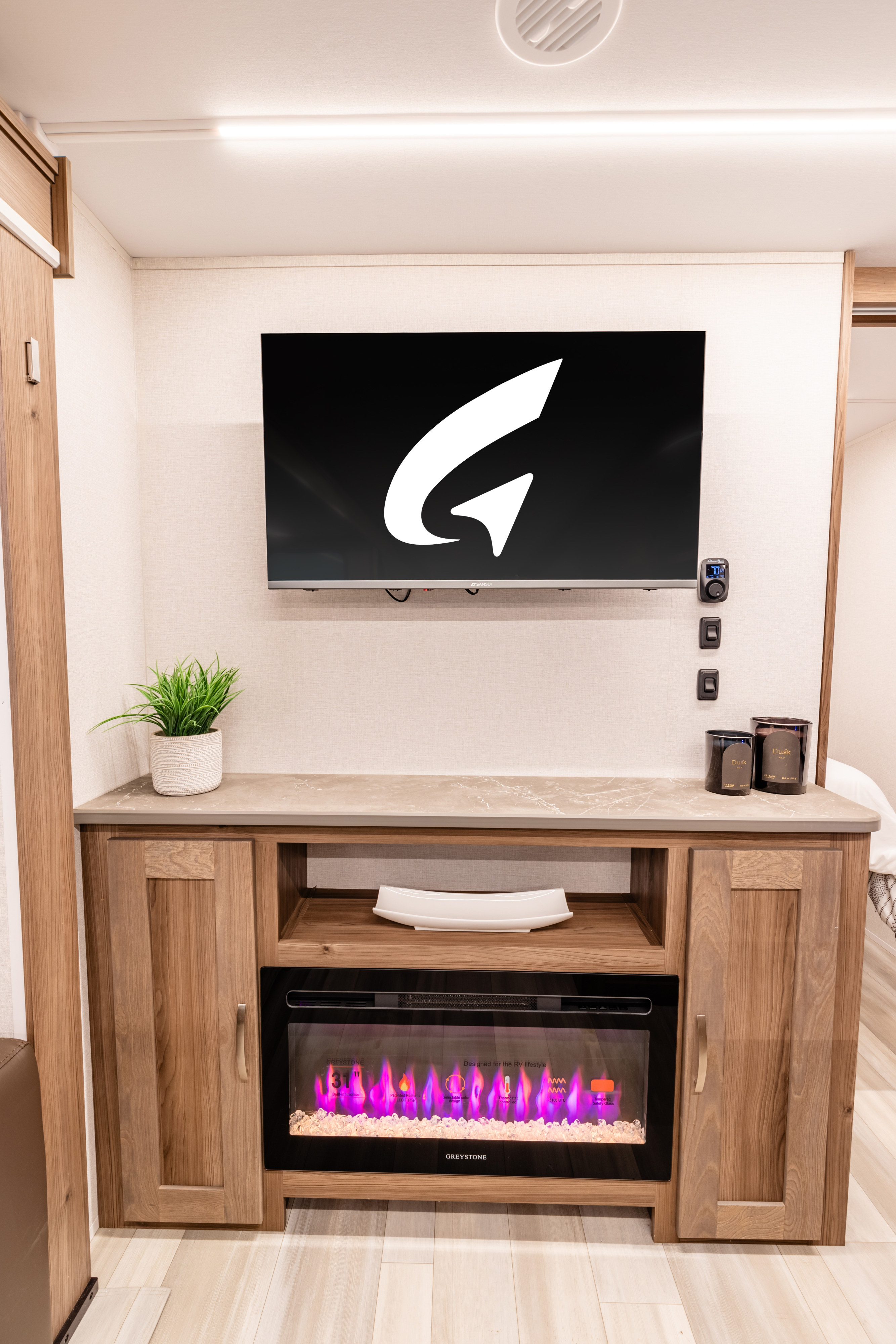 Modern RV rental living area featuring a wall-mounted TV above a wooden entertainment unit with a purple electric fireplace.. Go Explore X252 2025