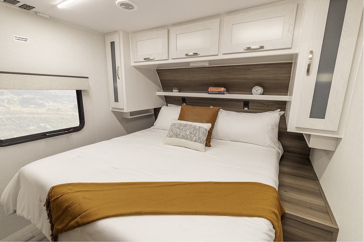 Comfortable RV rental bedroom with a large bed, overhead cabinets, and a window revealing an outdoor landscape.. Go Explore X252 2025
