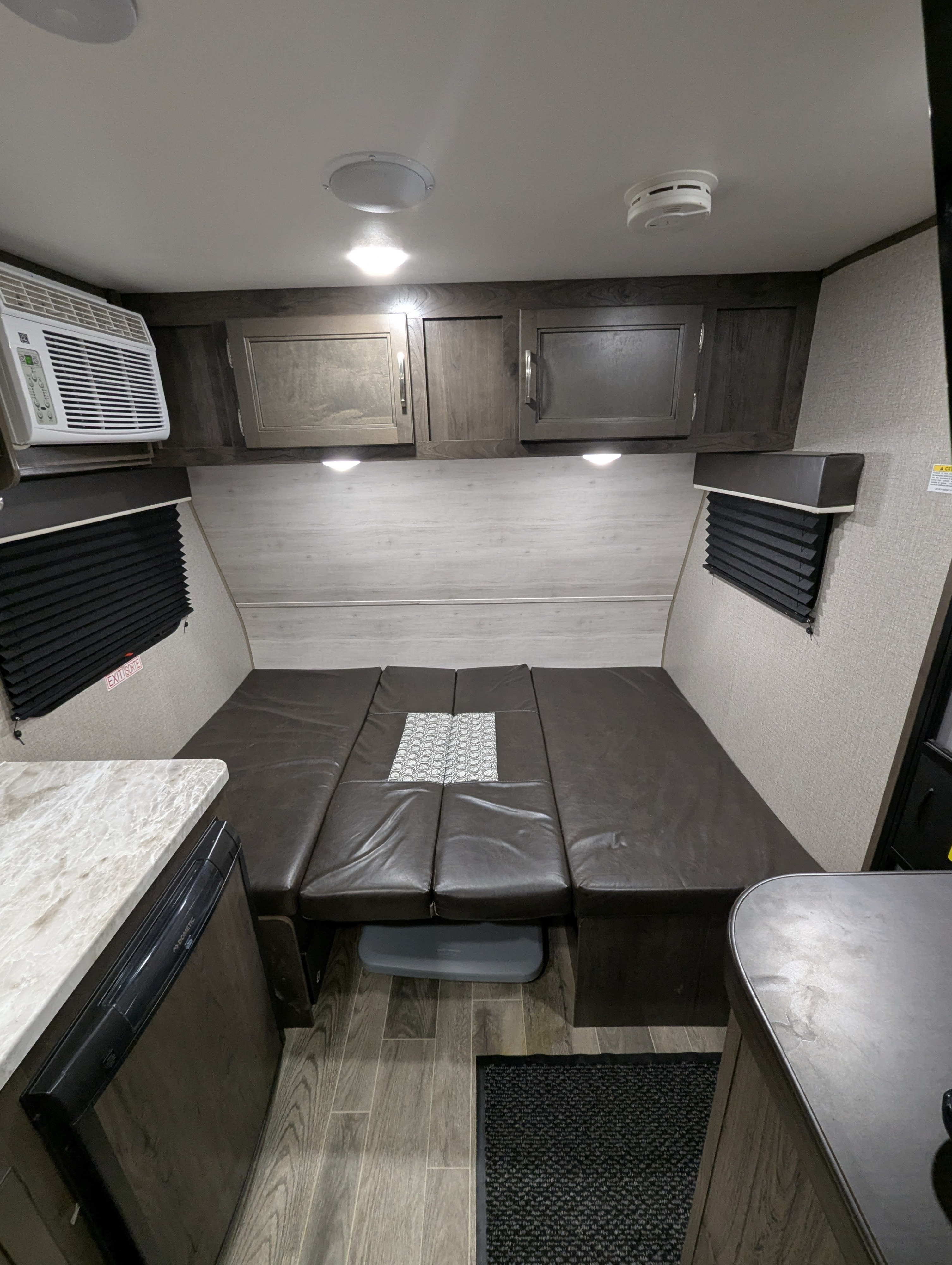 Interior of a compact RV rental, showcasing the convertible bed, overhead cabinets, AC unit, and part of the kitchen counter.. Jayco Jay Flight SLX 2021
