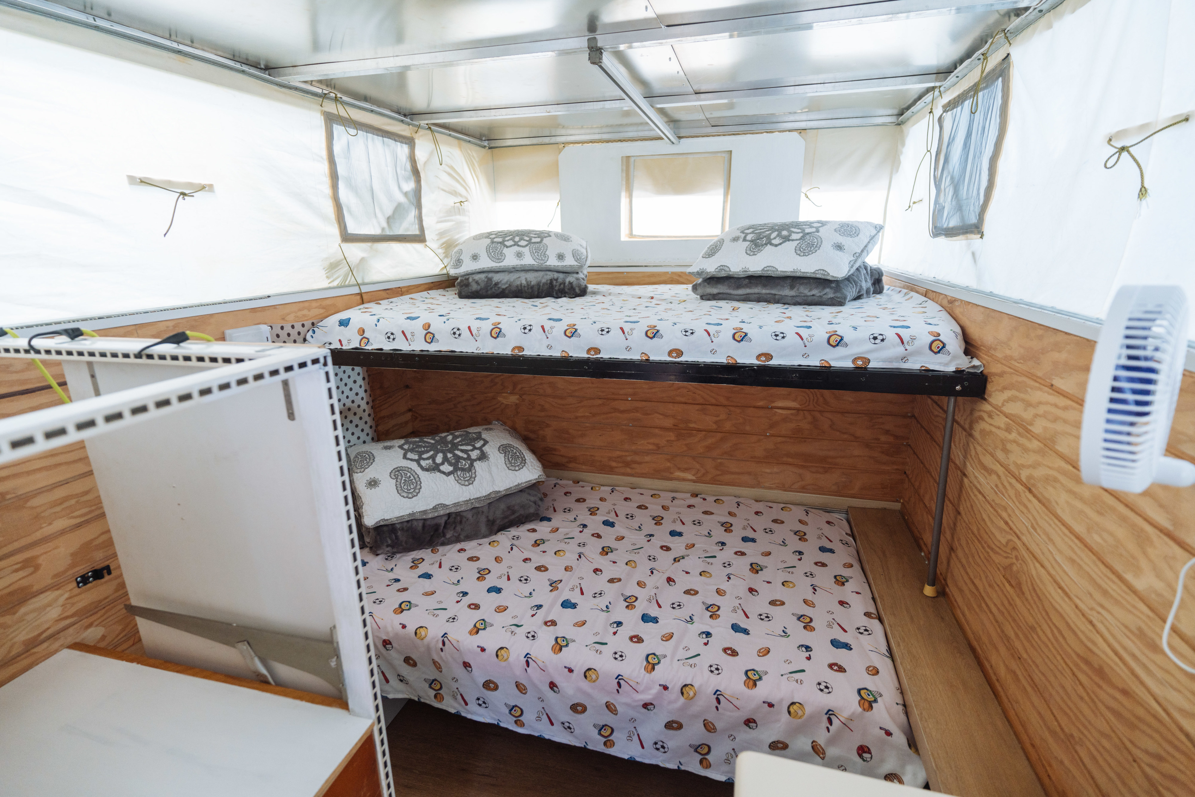 Cozy RV rental bunk beds with sports-themed bedding inside a camper. Wooden walls and a fan make it comfortable for travel.. Ford Ford F150 2019