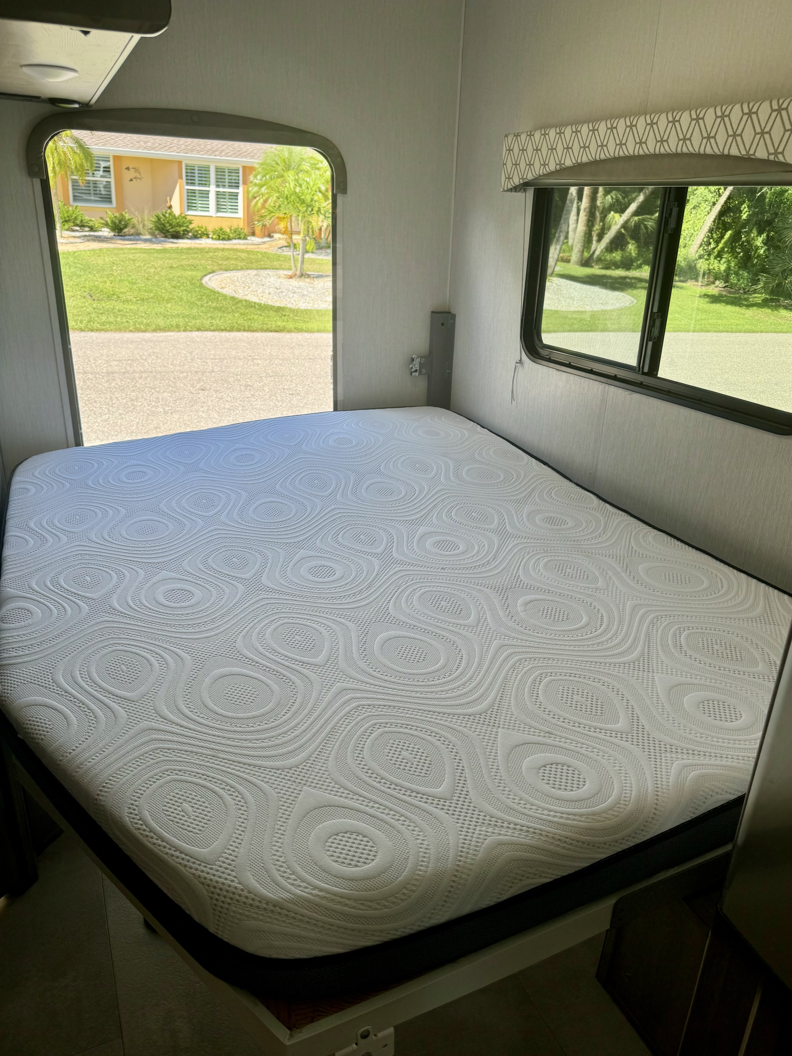 Clean, textured mattress in a bright RV rental bedroom, offering serene outdoor views of a house & palms.. Coachmen Freelander 2021