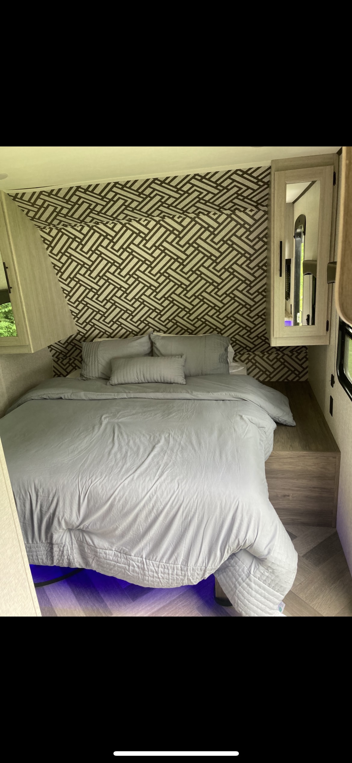 Inside an RV rental: a modern bedroom with a comfortable bed, stylish geometric wall, and inviting blue ambient light.. Crossroads RV Zinger 211RD 2024