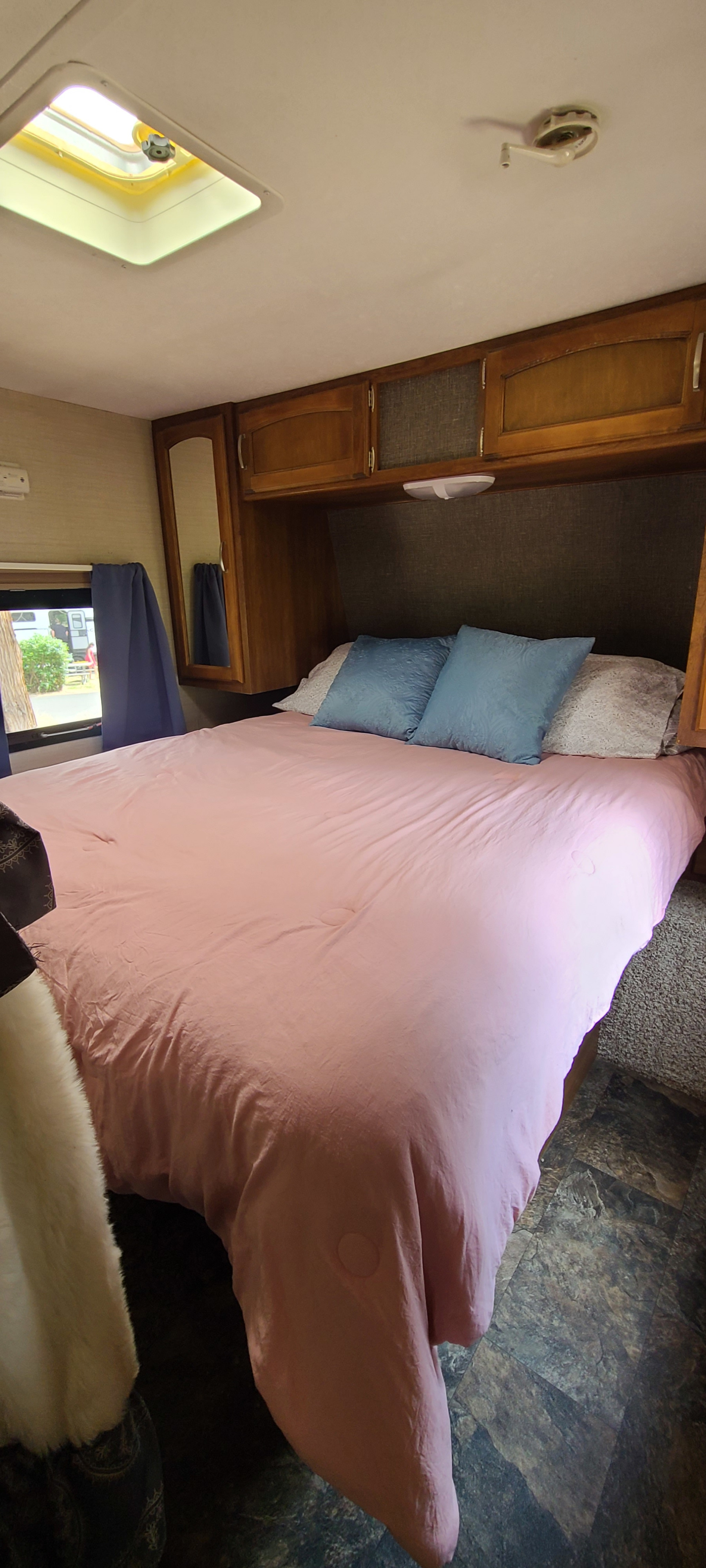 RV rental bedroom with a comfy pink bed, blue pillows, wood cabinets, and a skylight. A cozy space for travel accommodations.. Keystone RV Springdale 2015