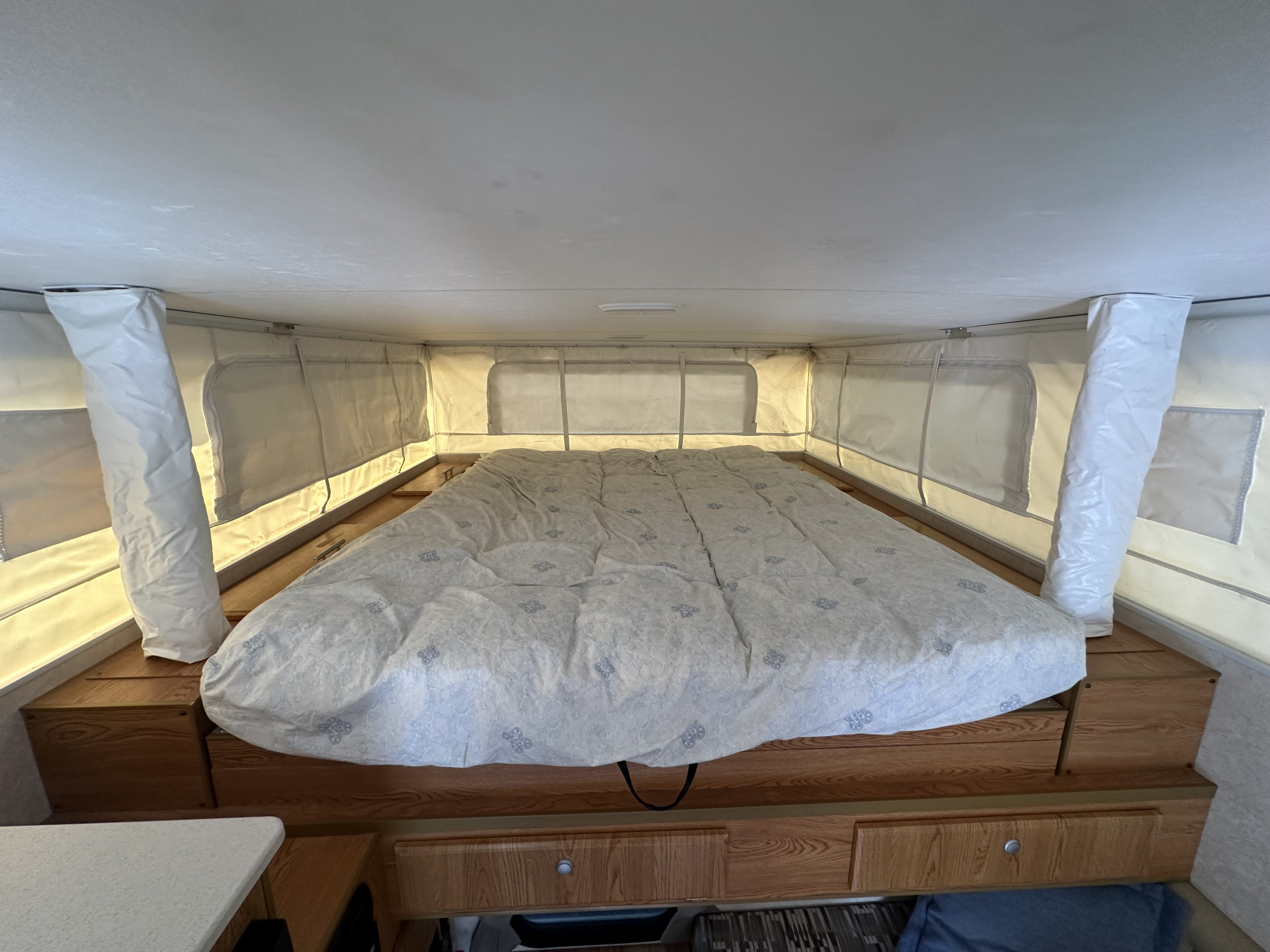 RV rental interior shows a spacious bed with patterned duvet, wood cabinetry, and fabric pop-up walls, ready for camping.. Bunkhouse Camper Trailers Queen 2019