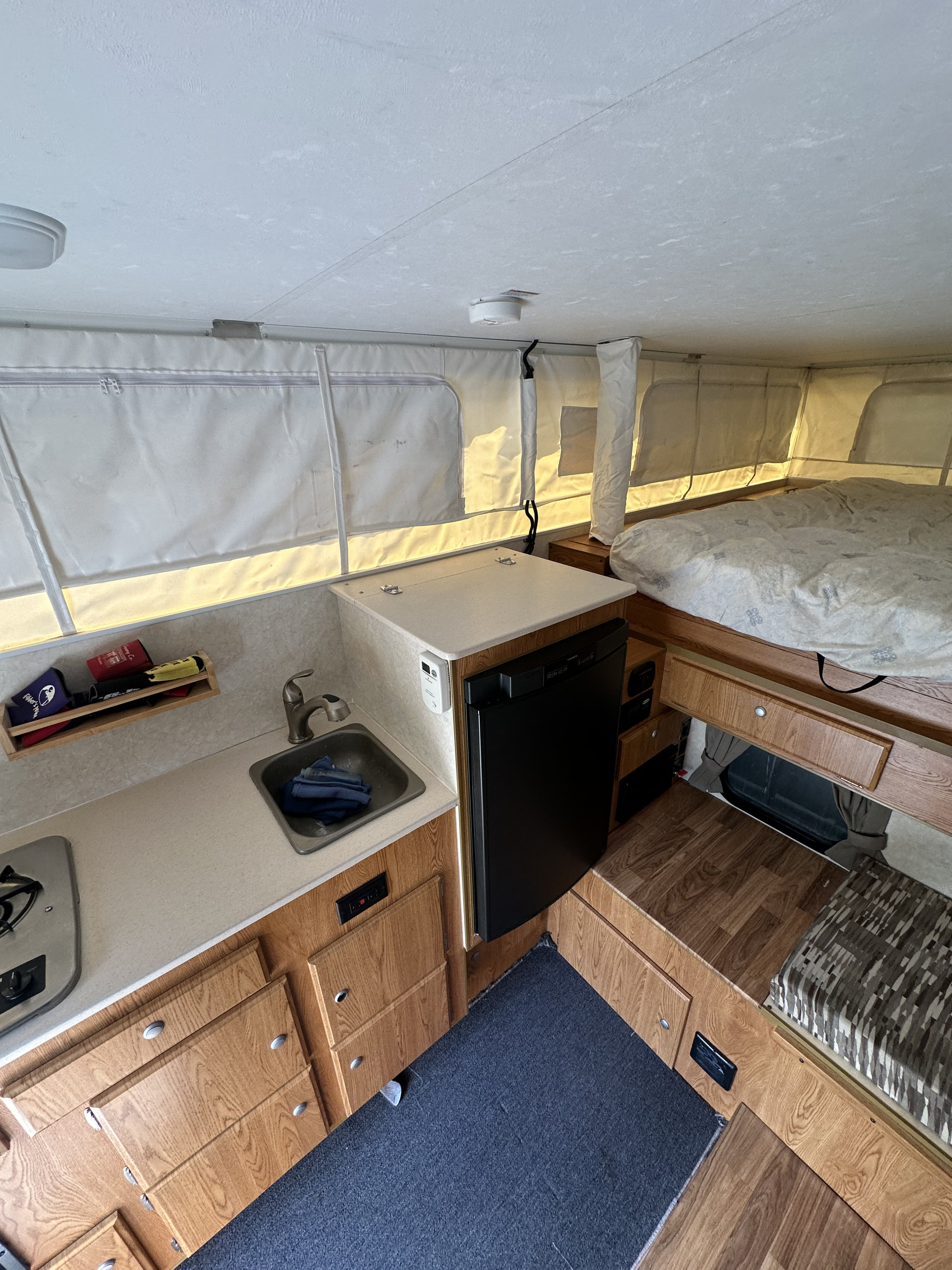 Inside this rv rental, a pop-up camper features a bed, kitchenette with sink/stove, fridge, and wooden storage.. Bunkhouse Camper Trailers Queen 2019
