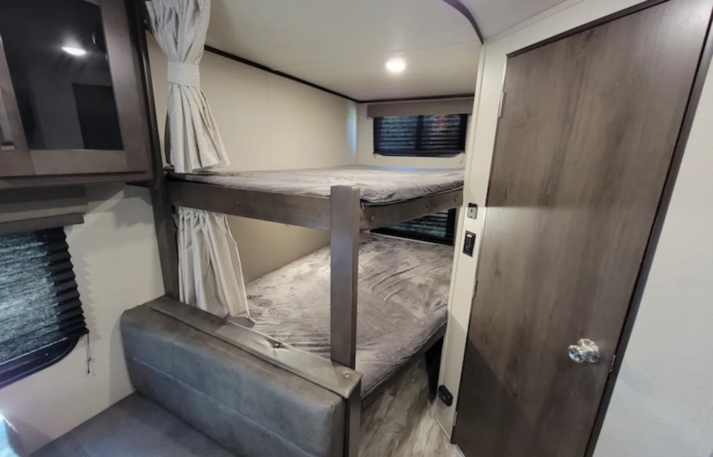 RV rental bunk beds with privacy curtains, cozy grey bedding, and a small seating area, ideal for compact camper living.. Grand Design Transcend Xplor 2023