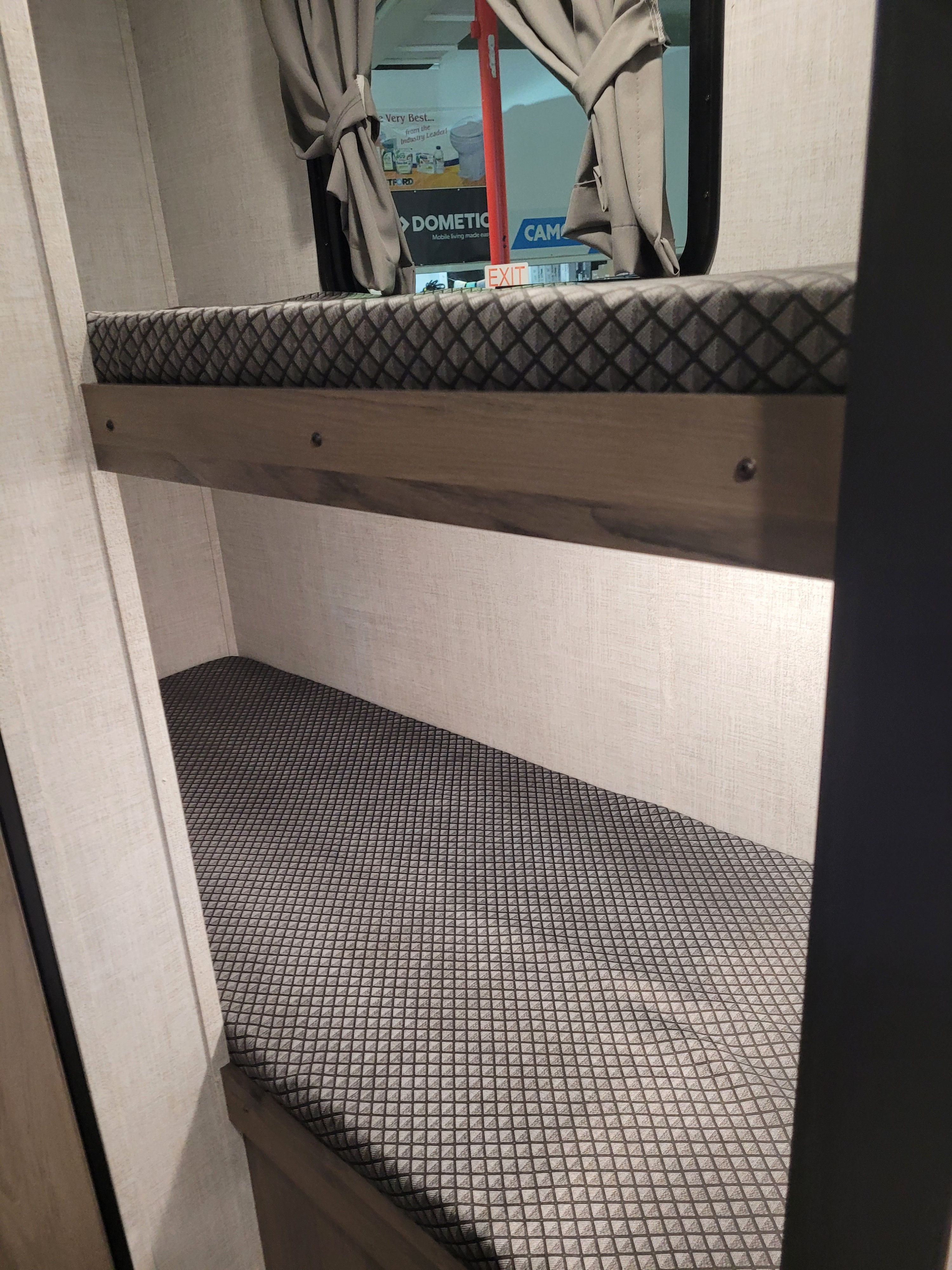 Cozy RV rental bunk beds, perfect for family travel. Diamond-pattern mattresses and a window view of an 'EXIT' sign.. Gulf Stream Ameri-Lite Super Lite 2022