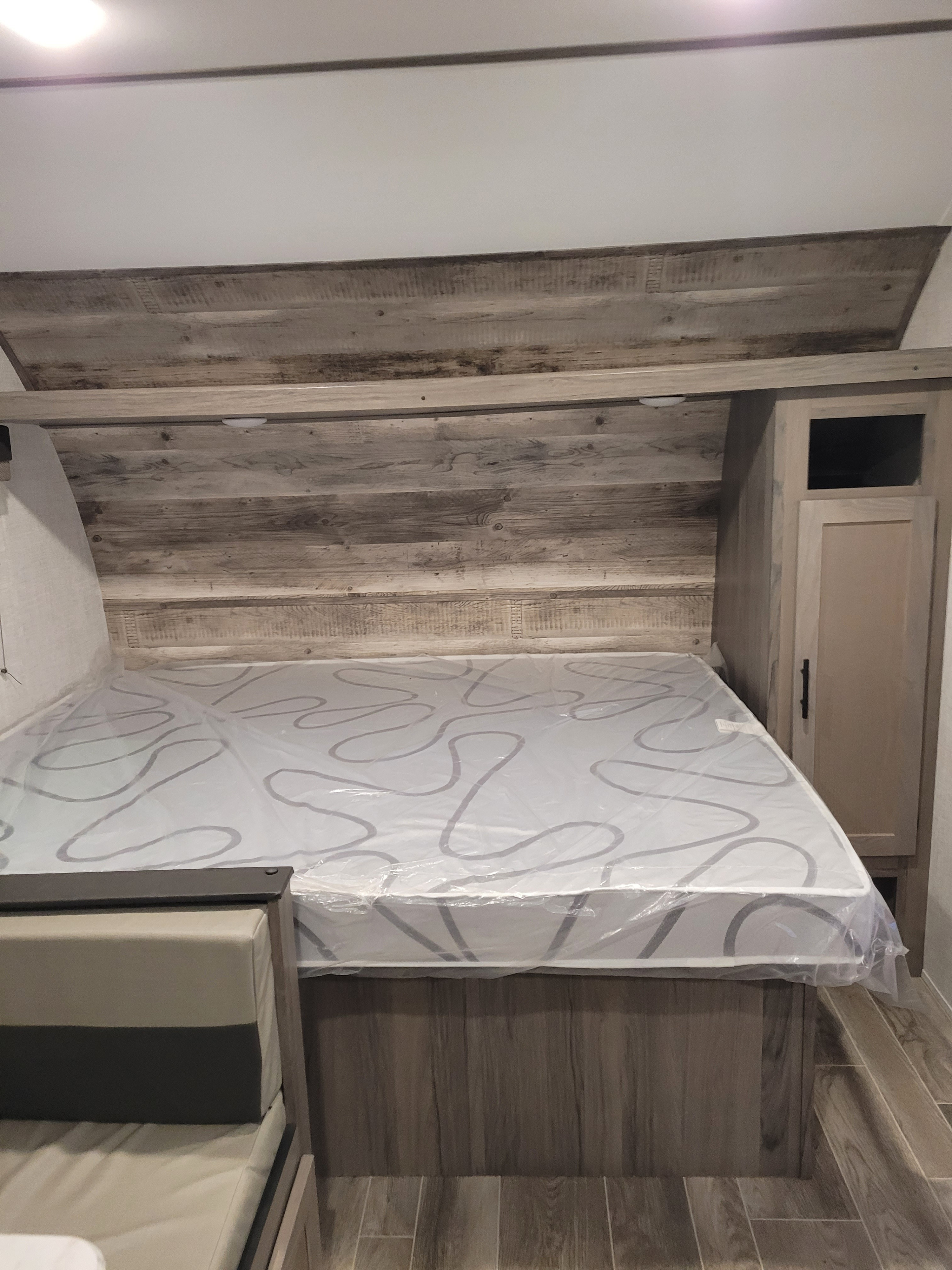 Cozy RV rental sleeping area with a new, plastic-wrapped mattress, distressed wood paneling, and cabinetry.. Gulf Stream Ameri-Lite Super Lite 2022
