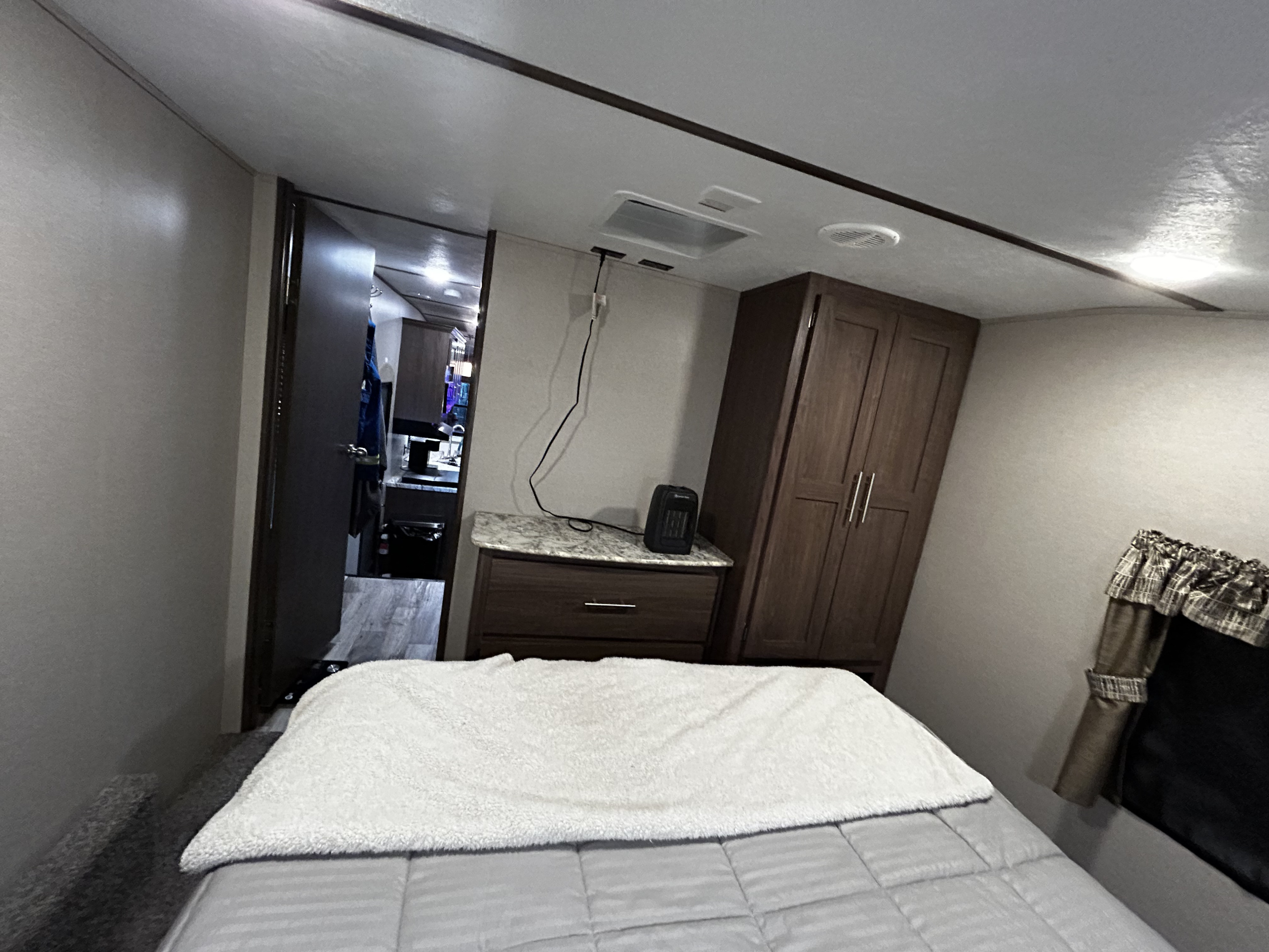 Compact RV rental bedroom with bed, heater, and wardrobe, leading to the living area.. Keystone RV Hideout 2019