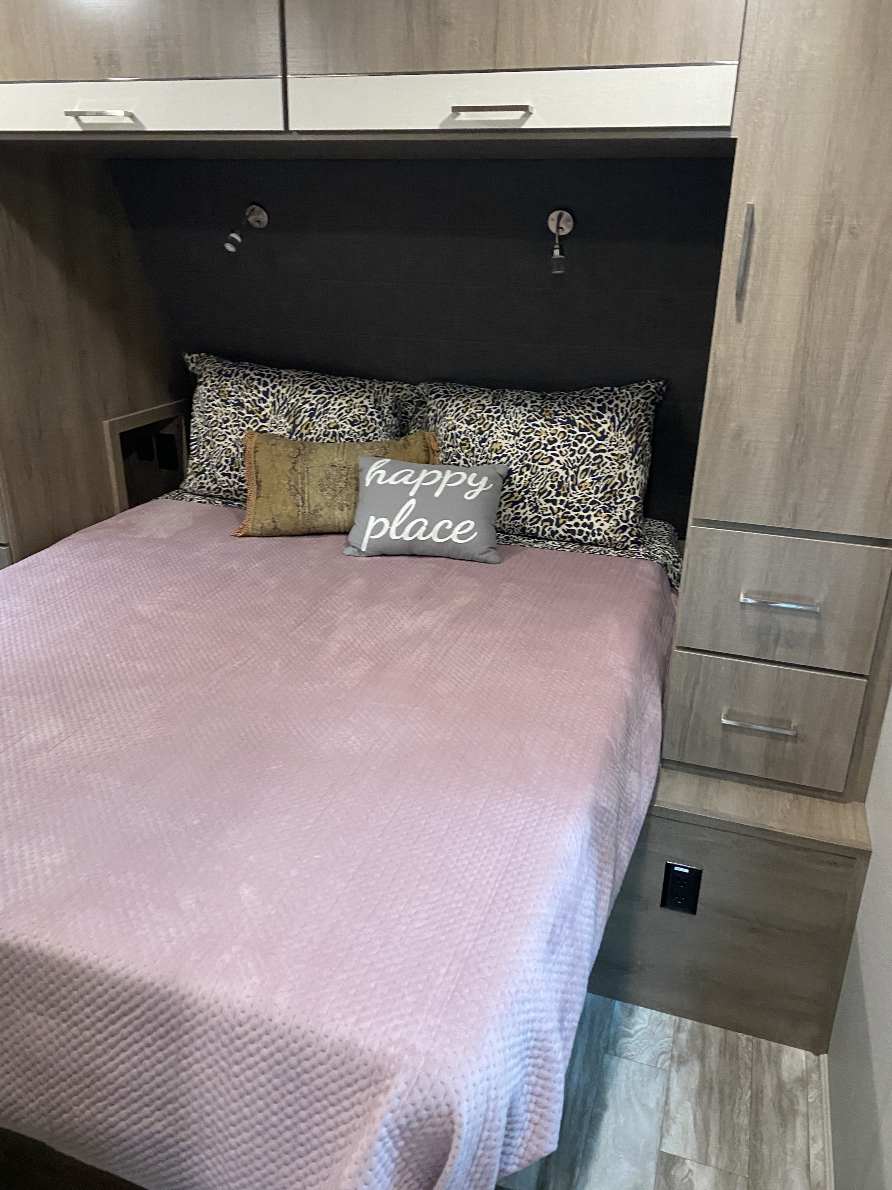 Cozy RV rental bedroom featuring a pink bed, leopard print pillows, "happy place" pillow, and built-in storage.. Grand Design Imagine 2021