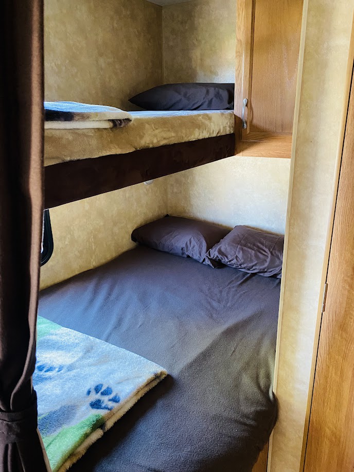 Inside an RV rental, two bunk beds feature dark bedding. The bottom bunk has a blue paw print blanket.. Jayco Jay Flight 2010