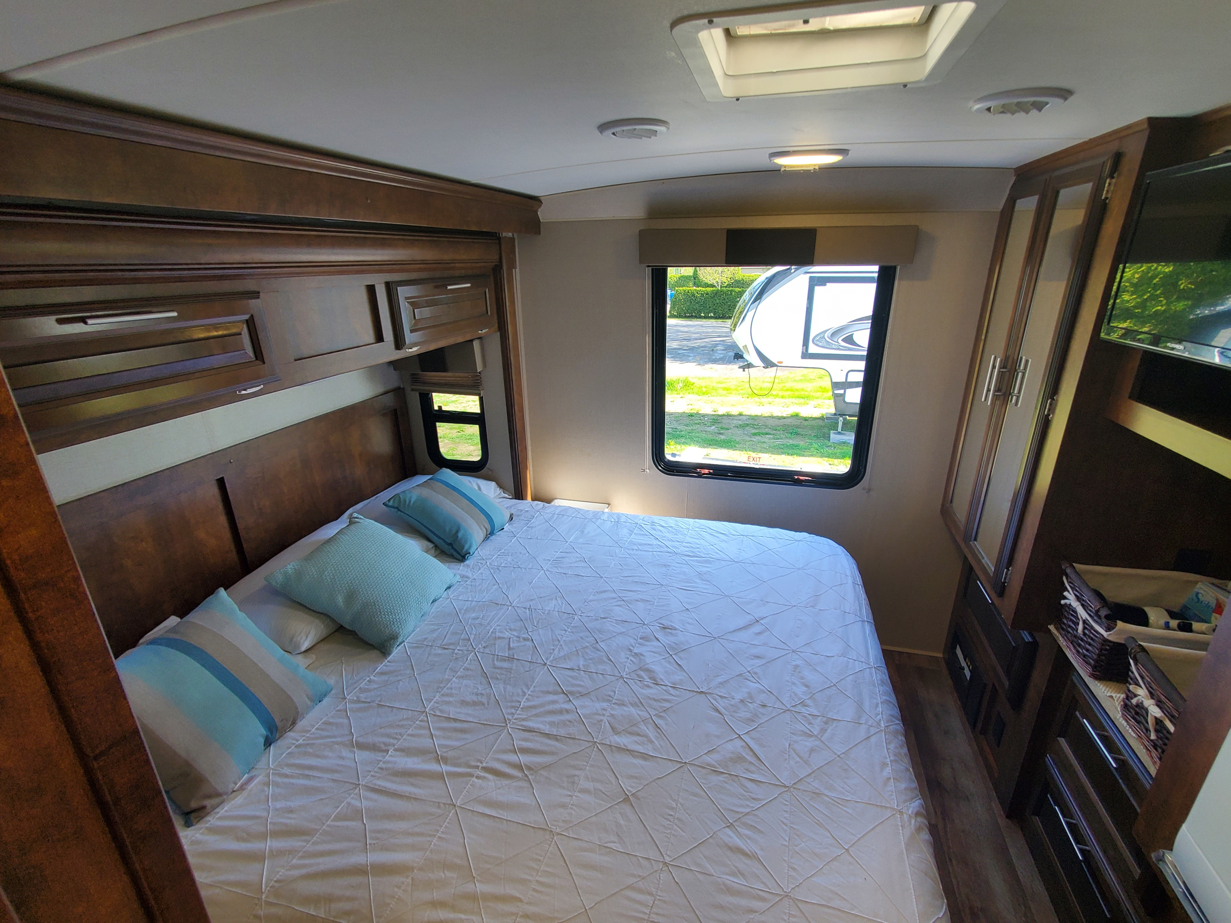 An RV rental bedroom with a large bed, light blue pillows, wooden cabinets, and a window view.. FR3 FR3 Motorhome 2017