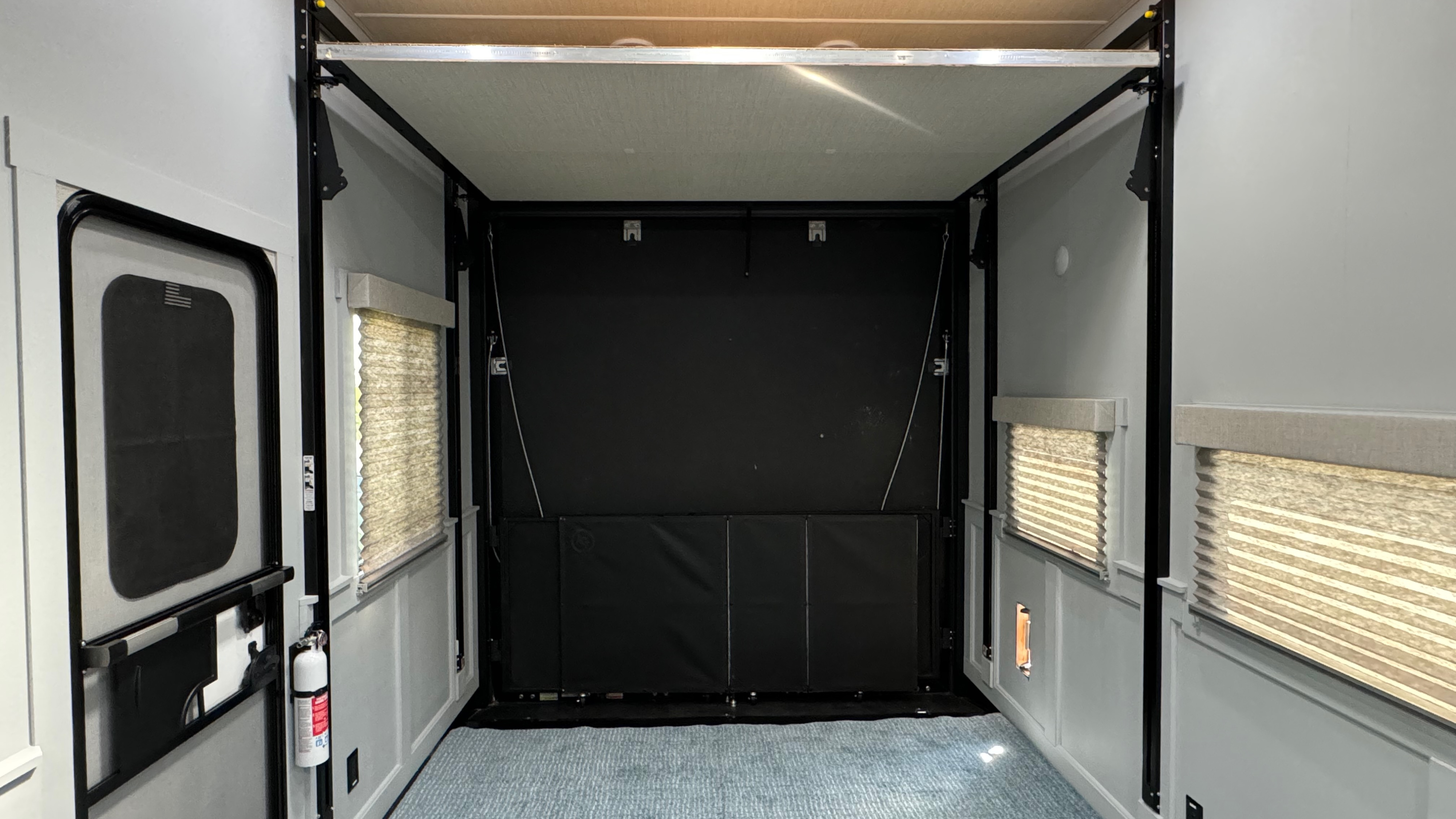 Clean rv rental toy hauler interior. Features a raised bed platform, black rear ramp door, light walls, and carpeted floor.. Grand Design Momentum 2022