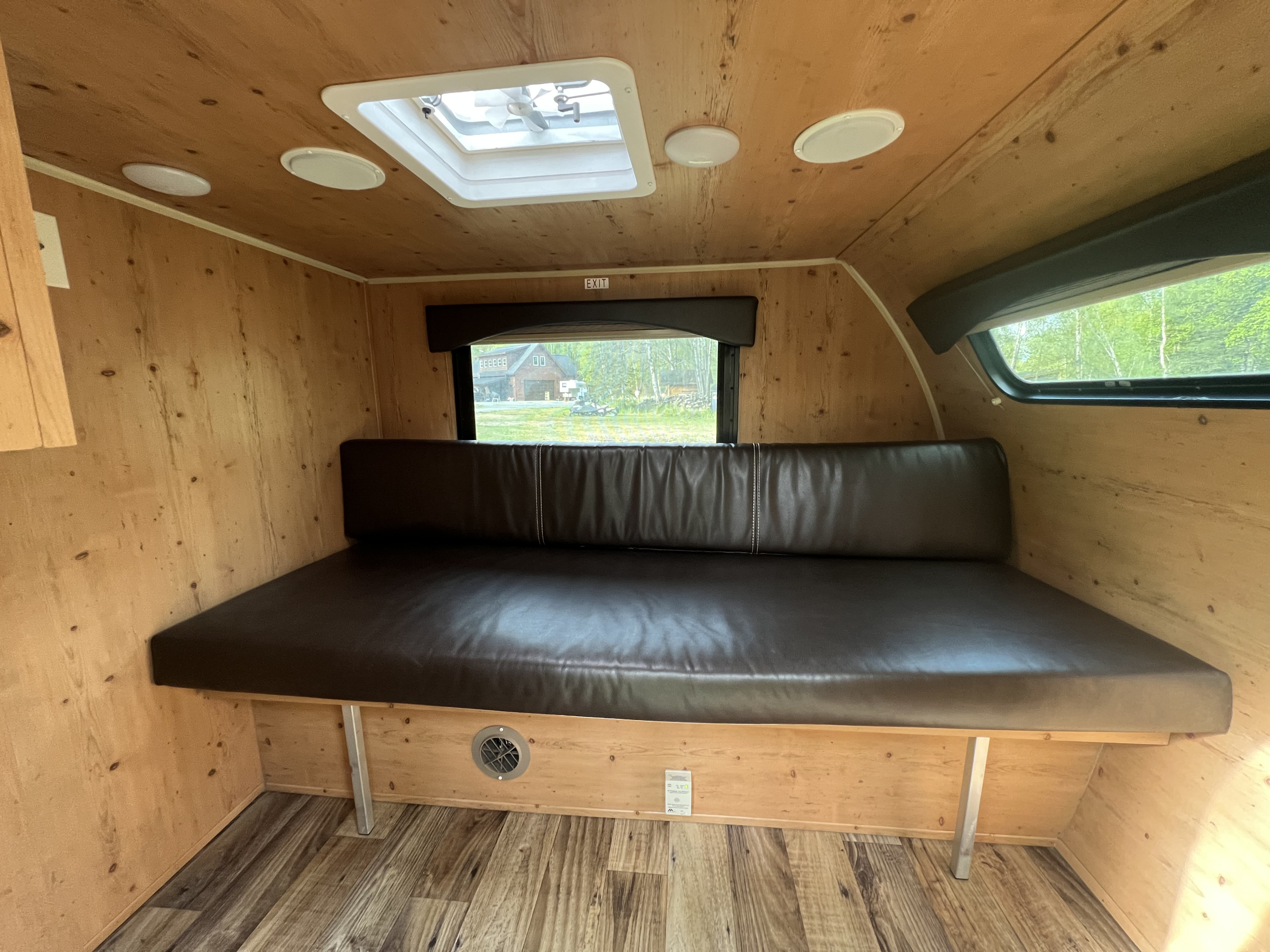 This cozy RV rental interior features warm wood paneling, a comfy brown bench seat, and a ceiling fan, offering a compact living space.. Sunset Park RV 109 2018