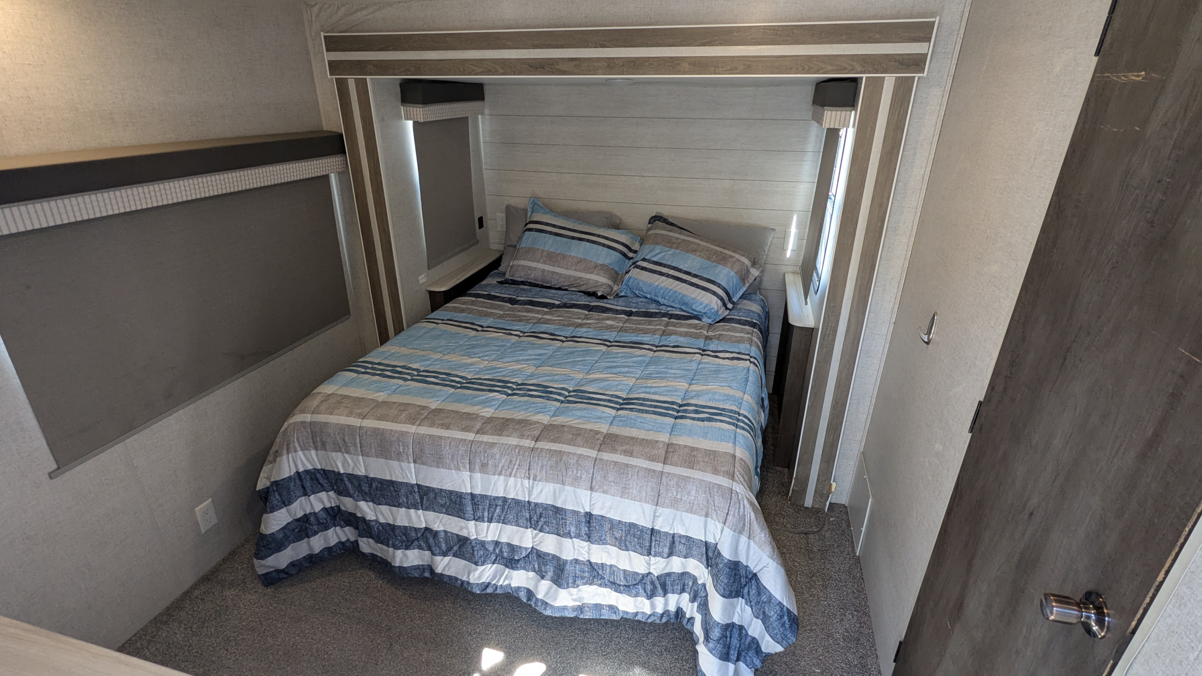 Cozy RV rental bedroom with a striped bed, built-in shelving, and large window blinds for privacy.. Forest River Salem 2021