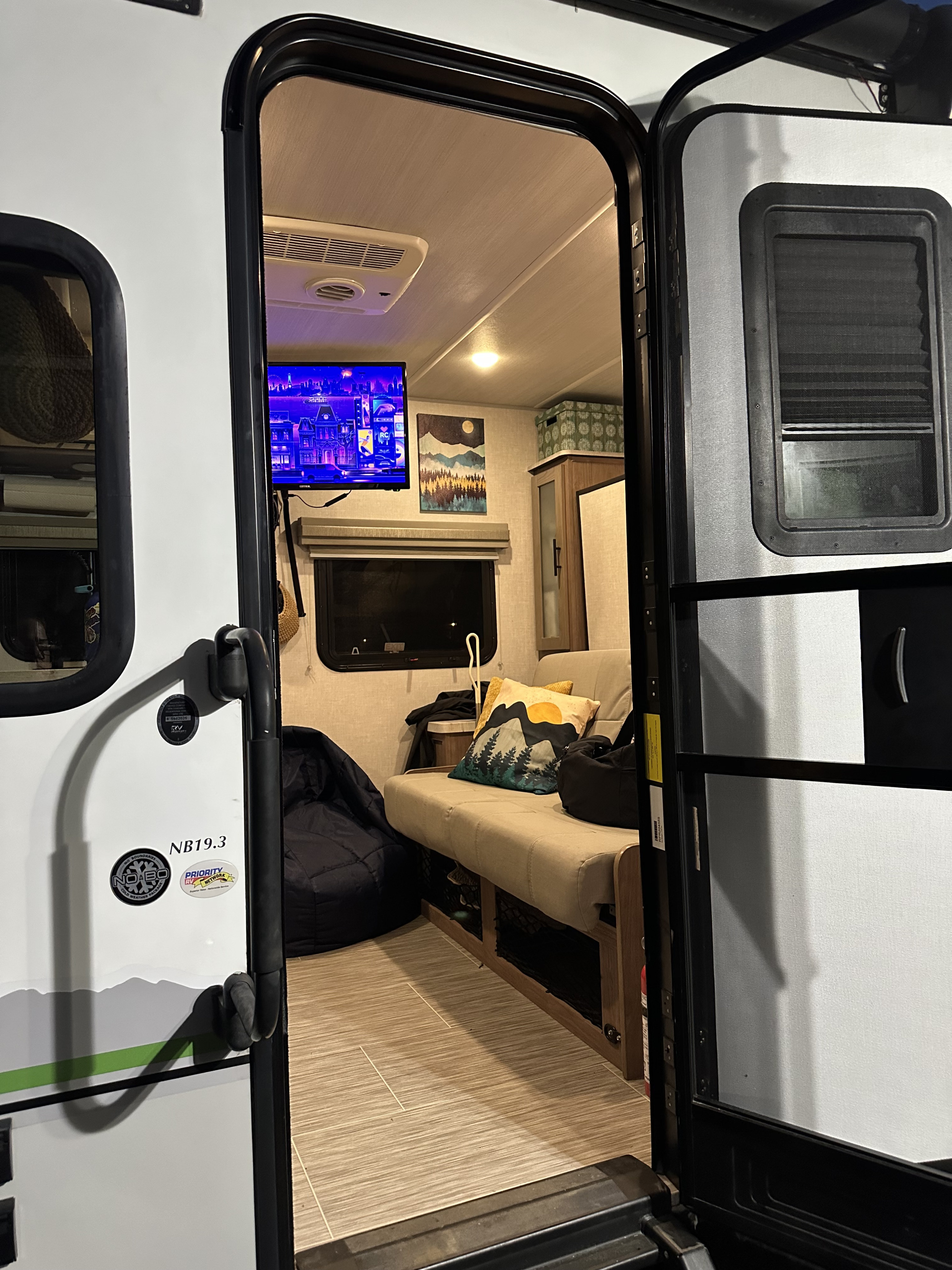 Cozy rv rental interior: sofa, TV, and beanbag chair visible from the open door. A comfy travel trailer living space.. No Boundaries 19 2021