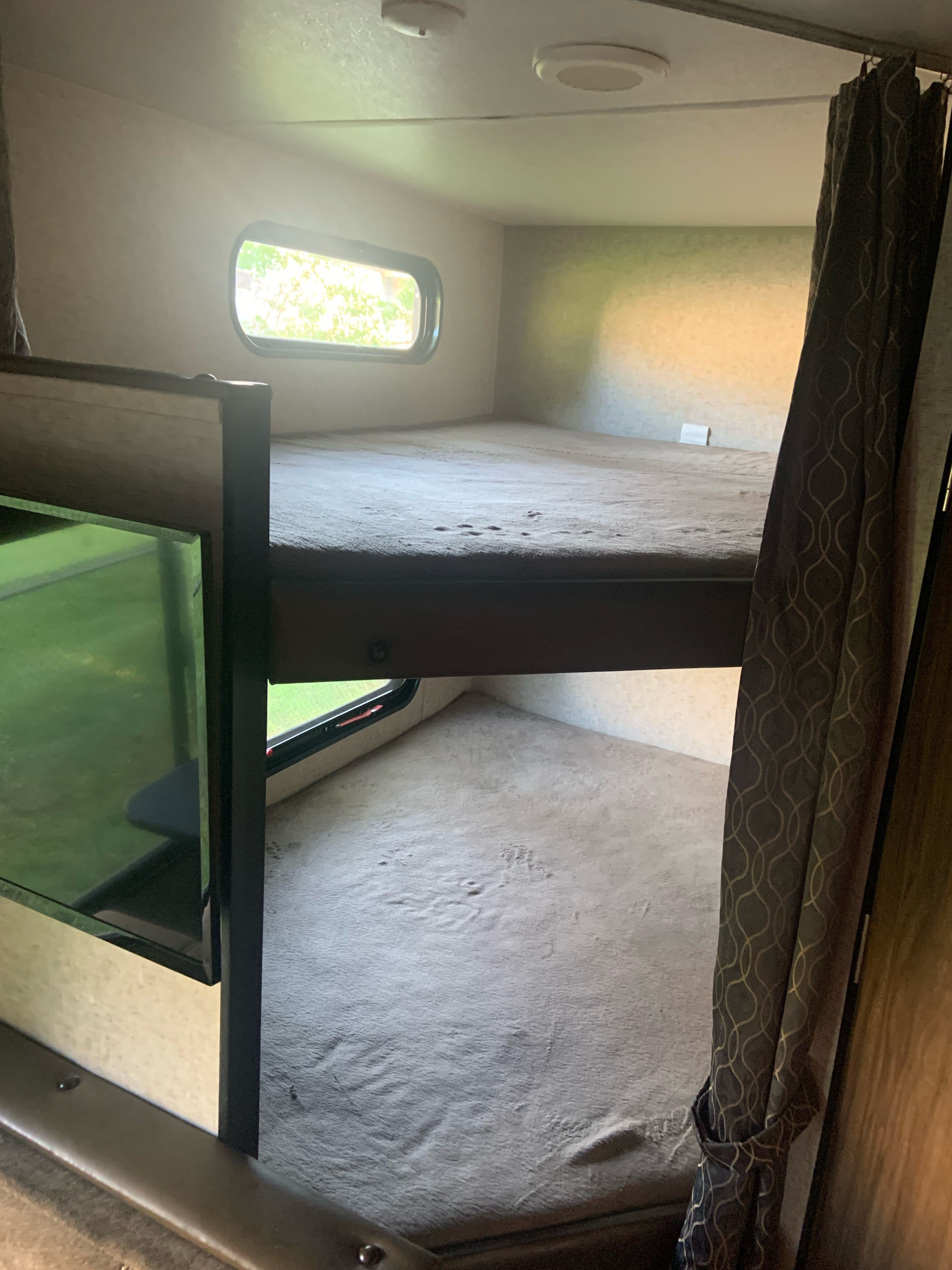 Inside an RV rental: two stacked bunk beds with soft grey sleeping areas, natural light from windows, and a TV. Ideal for a camper trip.. Forest River Cherokee Grey Wolf Special Edition 2019