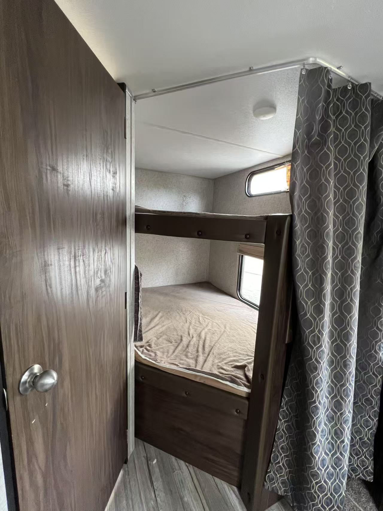 Inside an RV rental: a bunk bed sleeping area with two beds, small windows, and a privacy curtain, seen past an open door.. Forest River Cherokee 2018