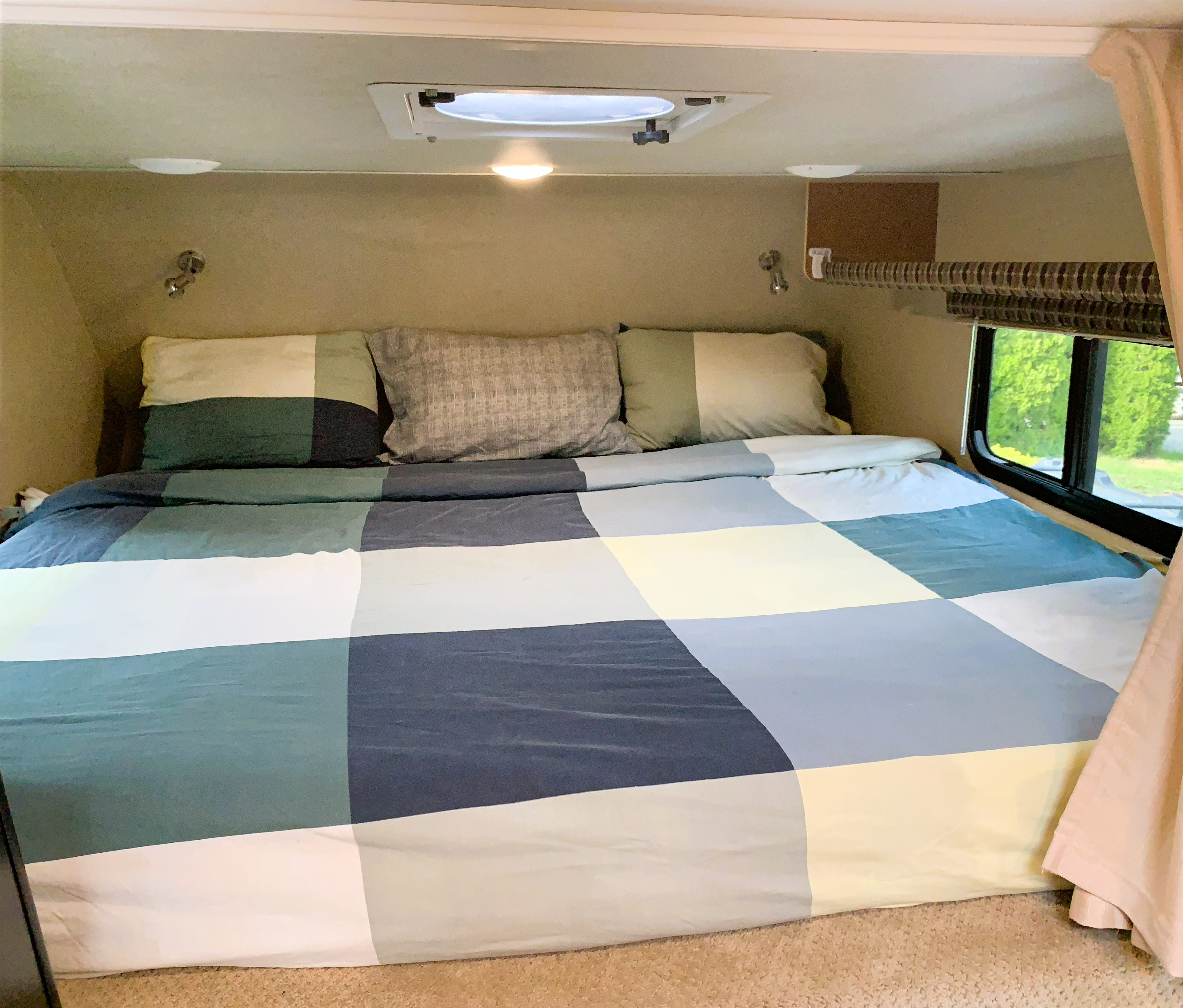 RV rental bedroom: comfortable bed with colorful checkered bedding, pillows, and a window offering an outside view.. RAM 3500HD 2016