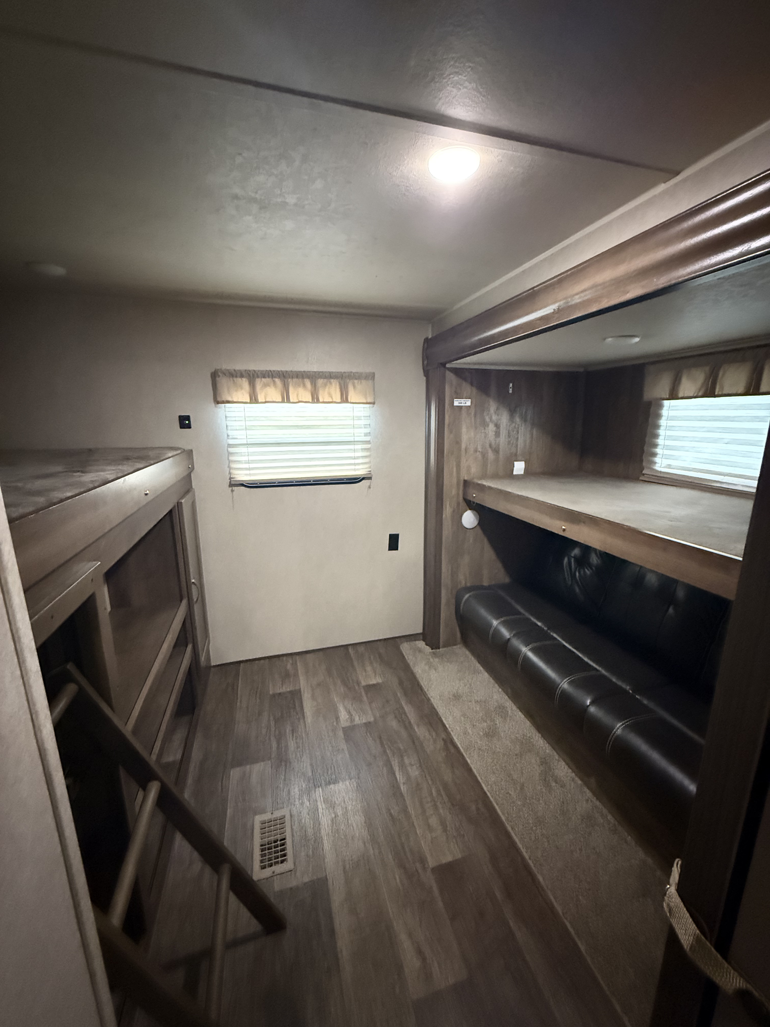 Cozy RV rental bunkhouse interior featuring dual bunk beds, a sofa, ladder, and natural light from a window.. Palomino 31bhss 2018