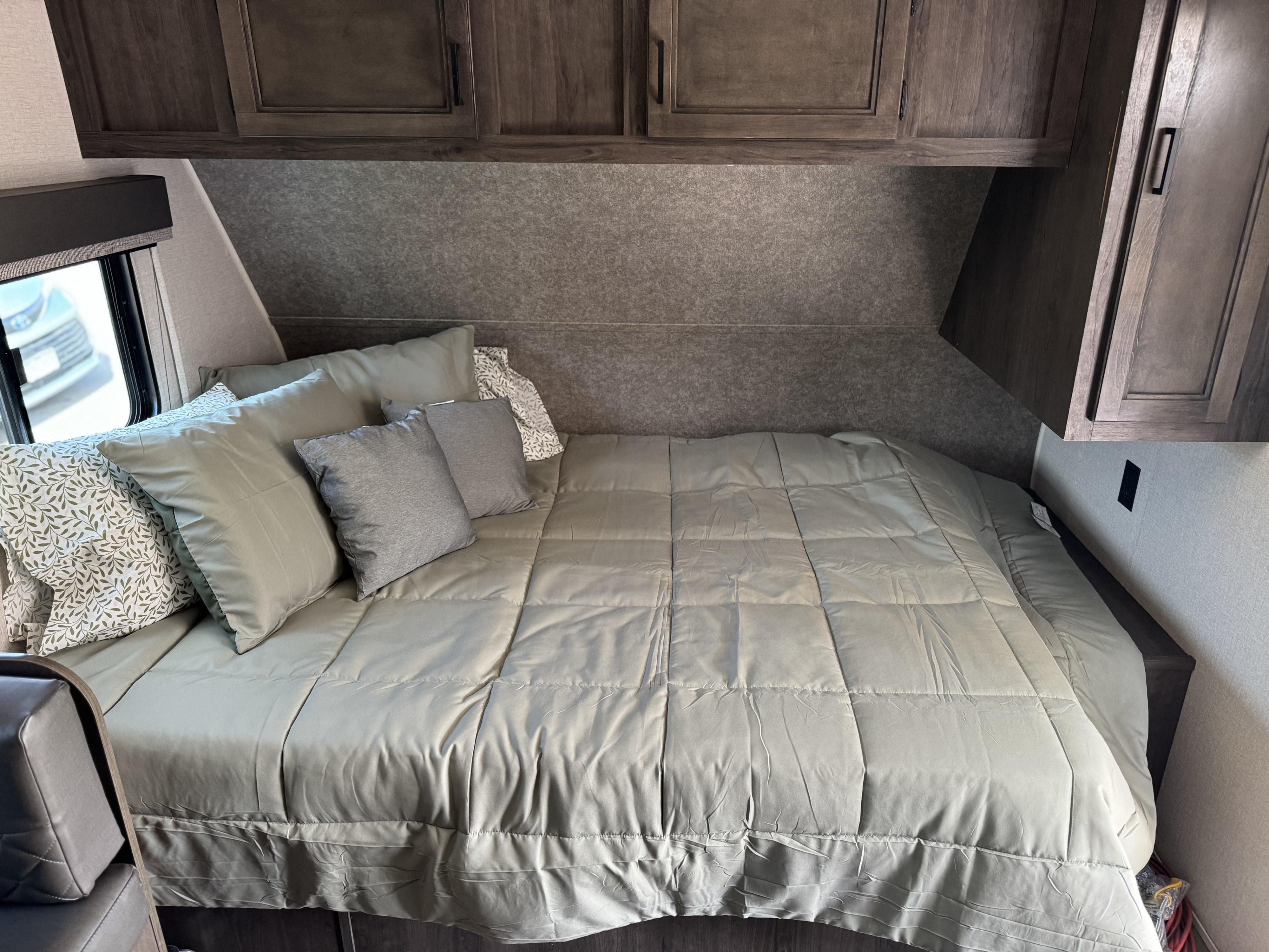 Inside an RV rental: a neatly made bedroom with a comfy bed, pillows, and functional overhead storage cabinets.. Starcraft Autumn Ridge 2021